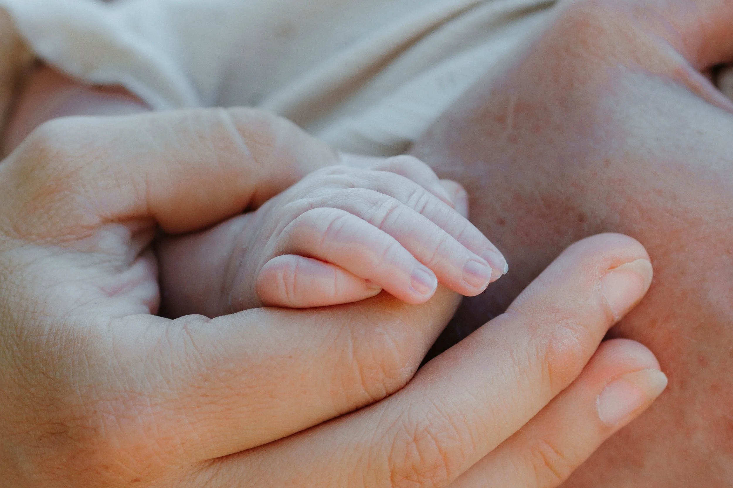 Nahaufnahme einer Erwachsenenhand, die ein Baby mit dem Daumen hält.