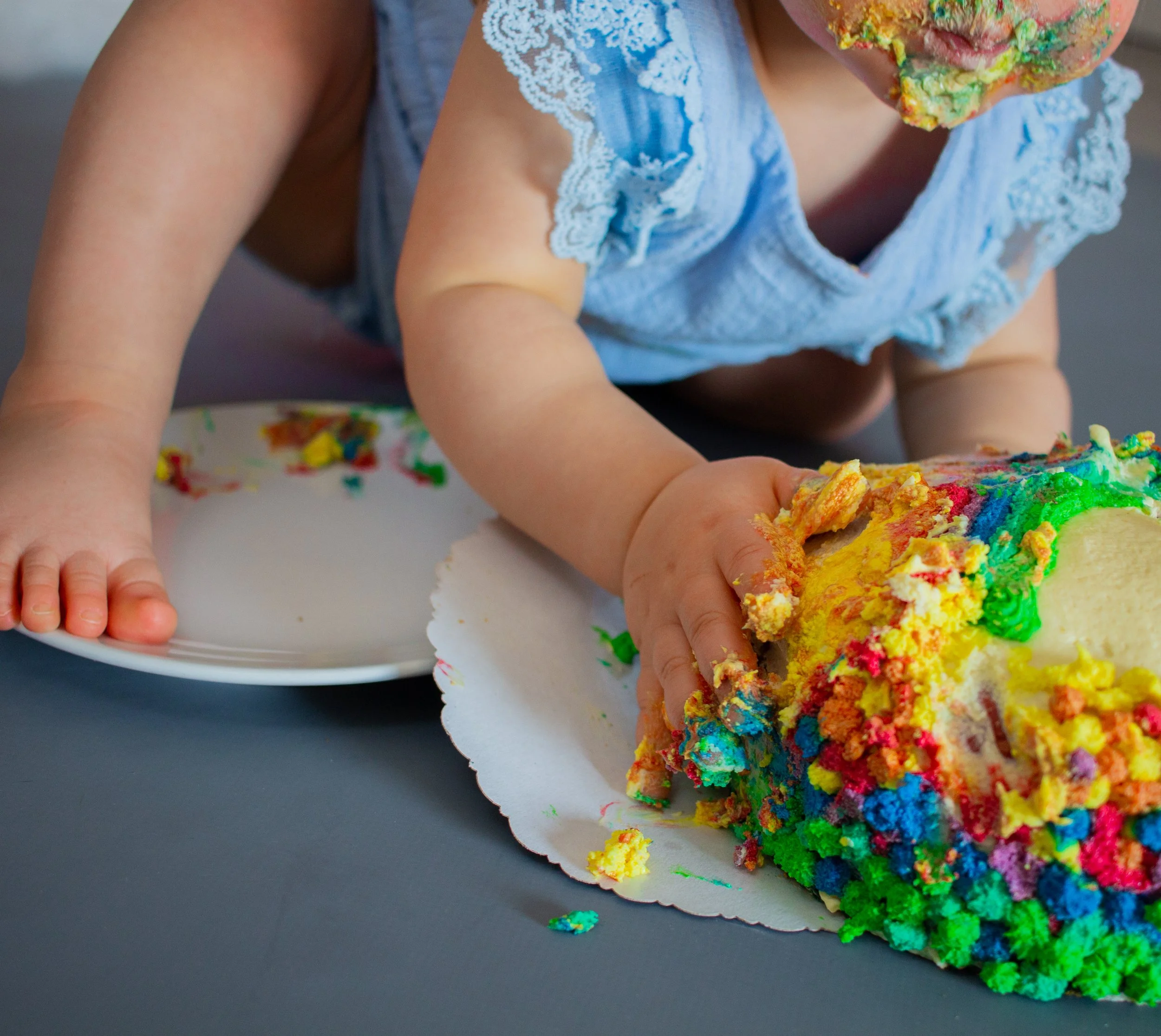 Kleines Kind bei einem Kindergeburtstag, das auf einem Tisch mit buntem, zerkrümeltem Kuchen spielt.