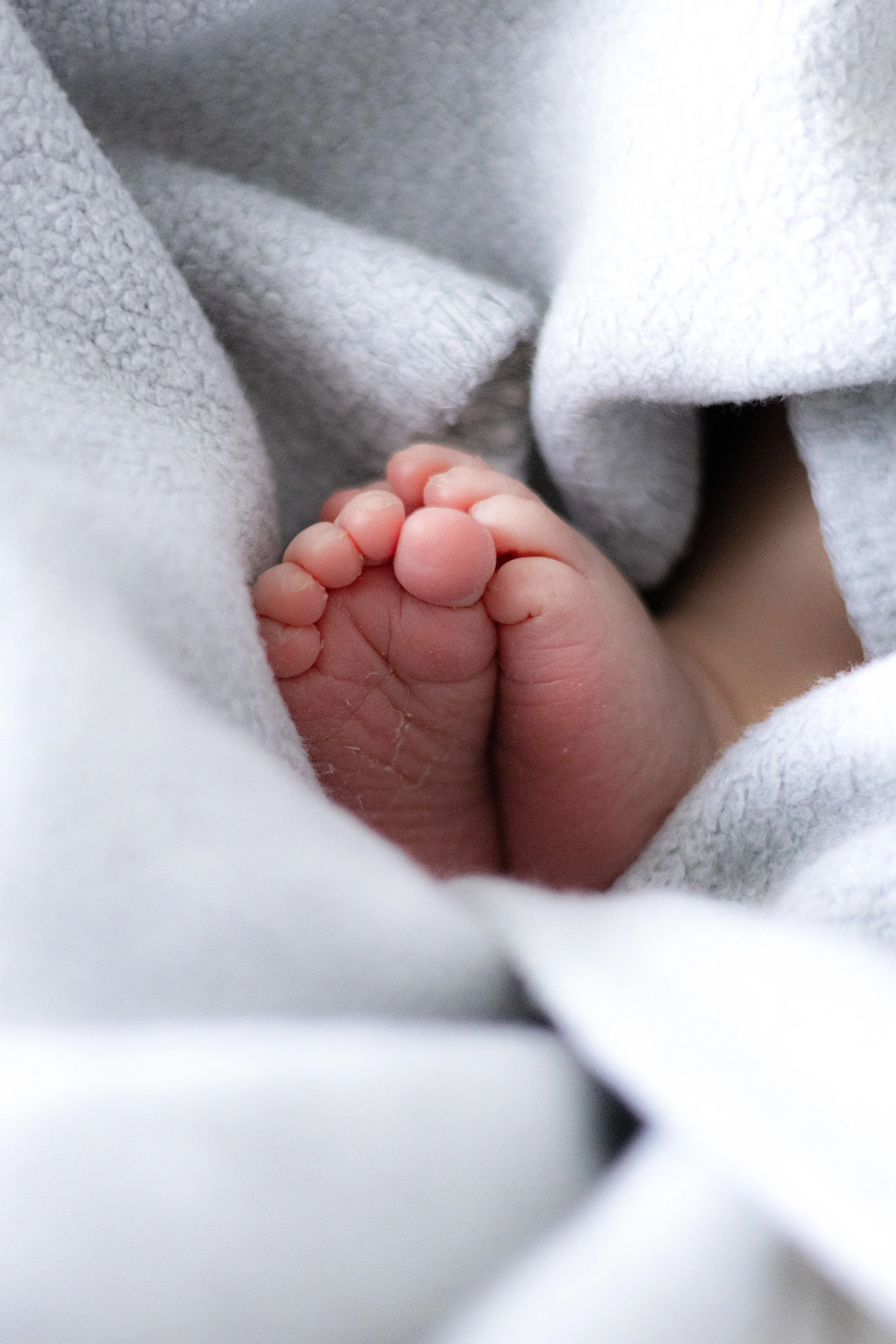 Naheaufnahme eines kleinen Baby-Füßchens, eingekuschelt in weiße Decken.