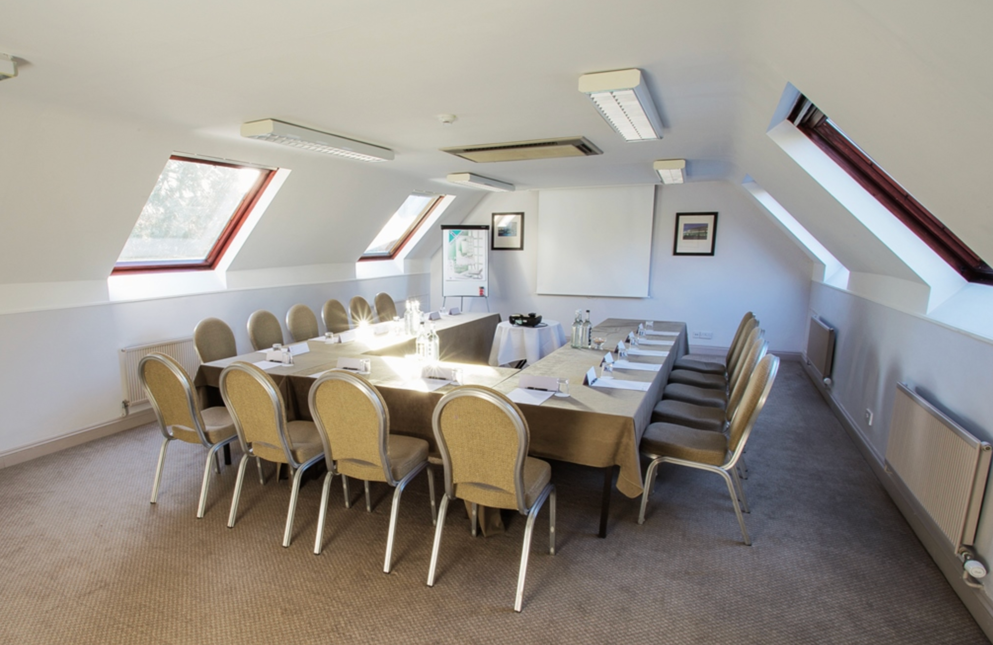 Conference room with U-shaped table arrangement, beige chairs, and skylight windows.