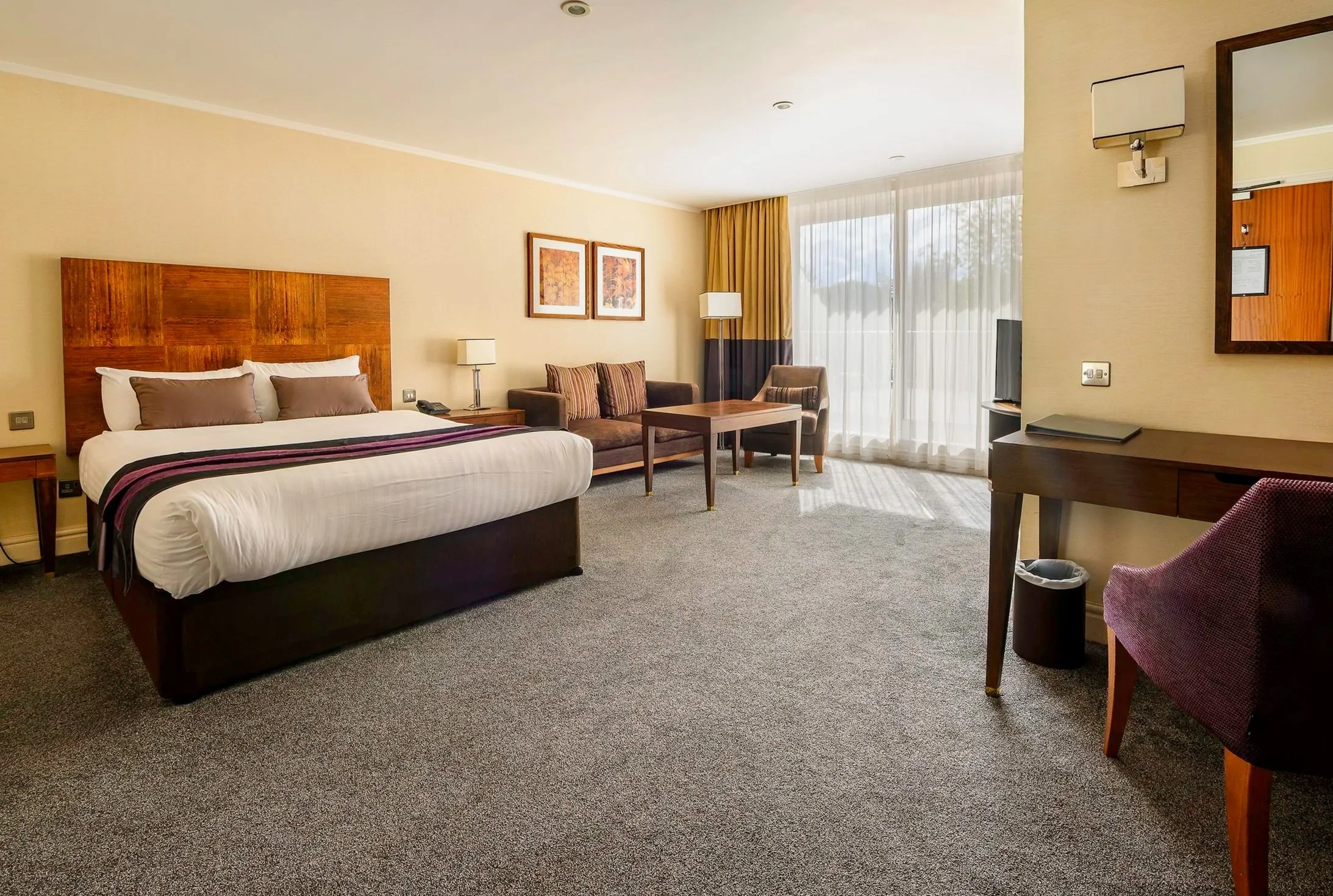 Hotel room with a large bed, sitting area, desk, and a view of a lake outside the windows.