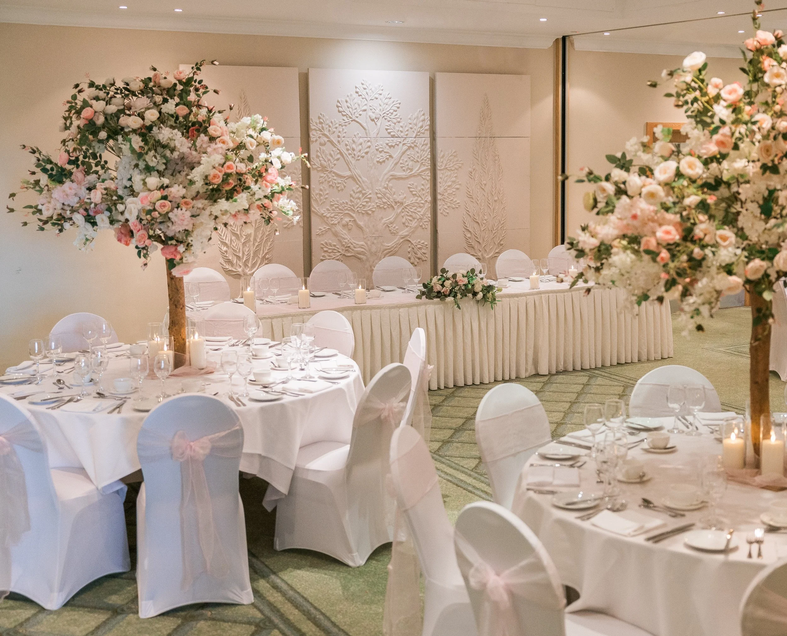 Elegant banquet hall decorated for a wedding reception with large floral centerpieces, white tablecloths, and neatly arranged tableware.