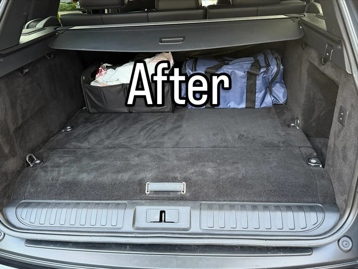 Empty car trunk with two bags, one black and one blue, positioned near the back seats. The trunk is clean and spacious, with a retractable cargo cover partially visible.