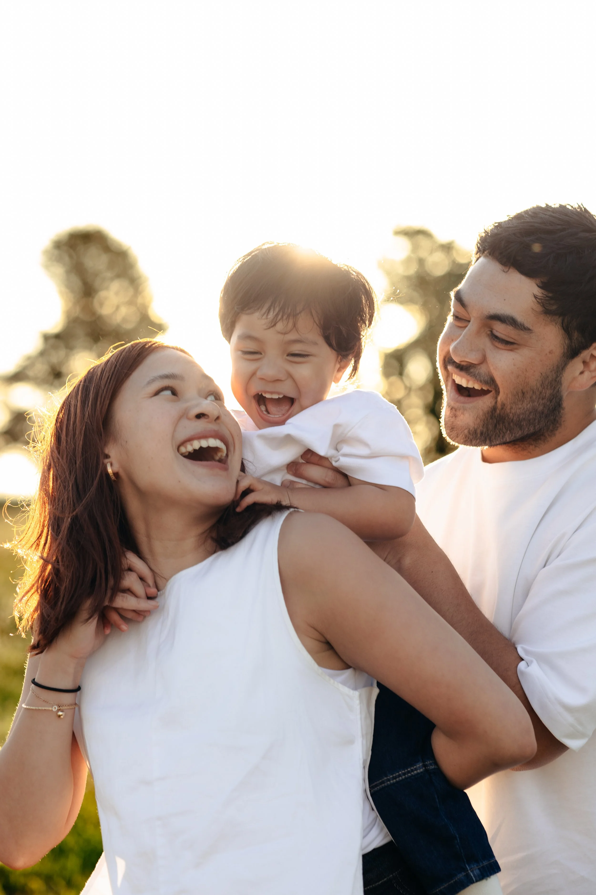 Family of 3 with a young child on mums back, smiling in the sun