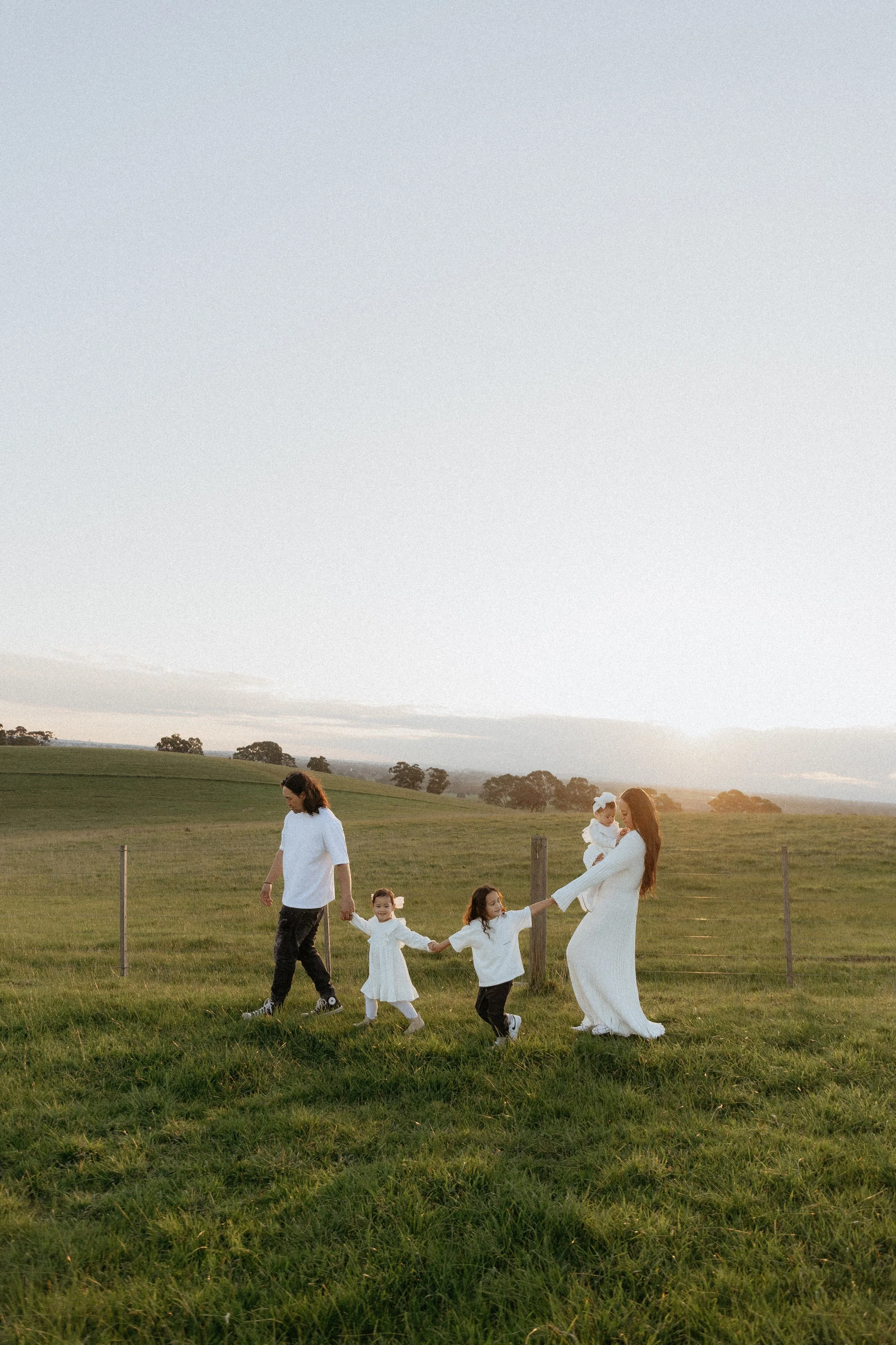 Family of 5 holding hands and walking in a field with beautiful sunsets in the background