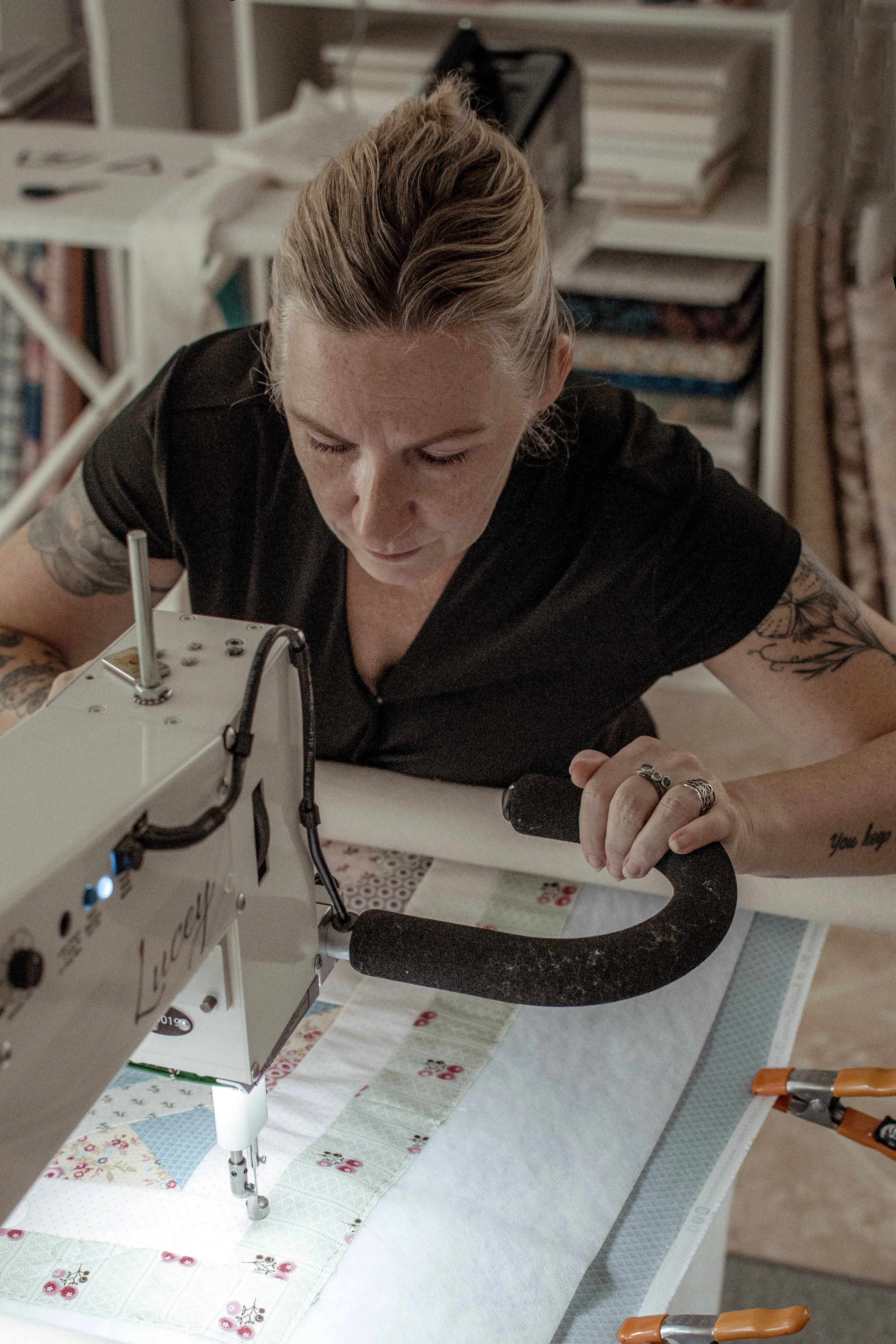 A woman with tattoos sewing a fabric with a quilting machine.