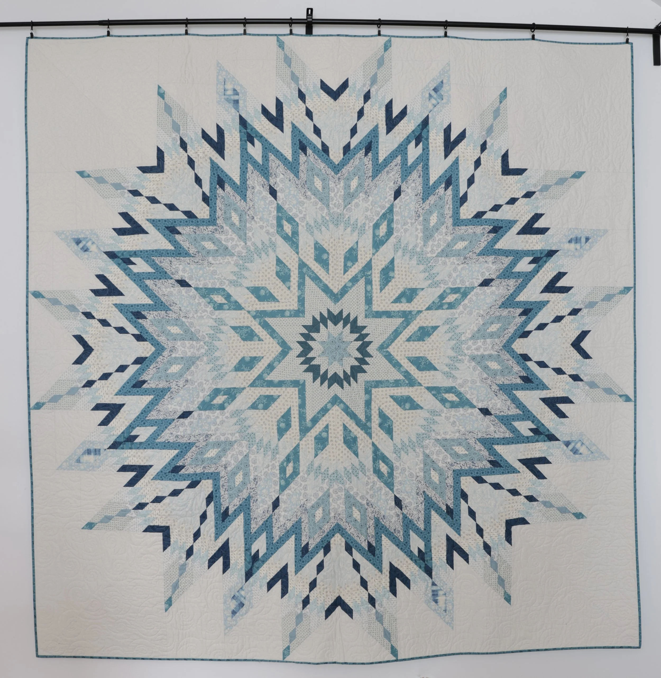 A quilt with a snowflake pattern in various shades of blue and white.