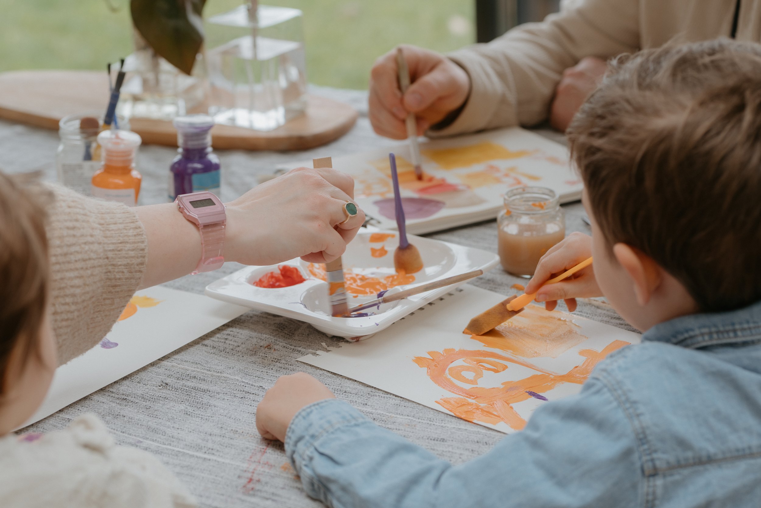Une scène de peinture où une famille travaille ensemble sur des créations artistiques avec des pinceaux, de la peinture de différentes couleurs et du papier.