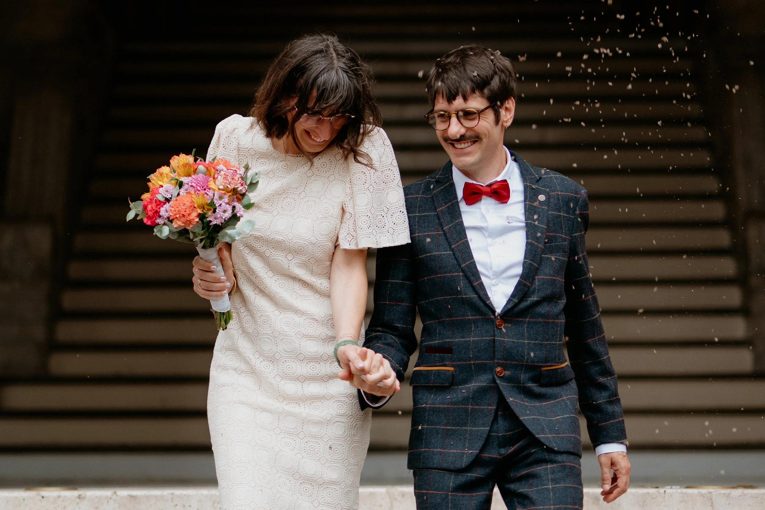 Un couple souriant lors de leur mariage dans les Hauts-de-Seine, main dans la main, la mariée portant une robe blanche avec un bouquet de fleurs colorées, sortie de la mairie.