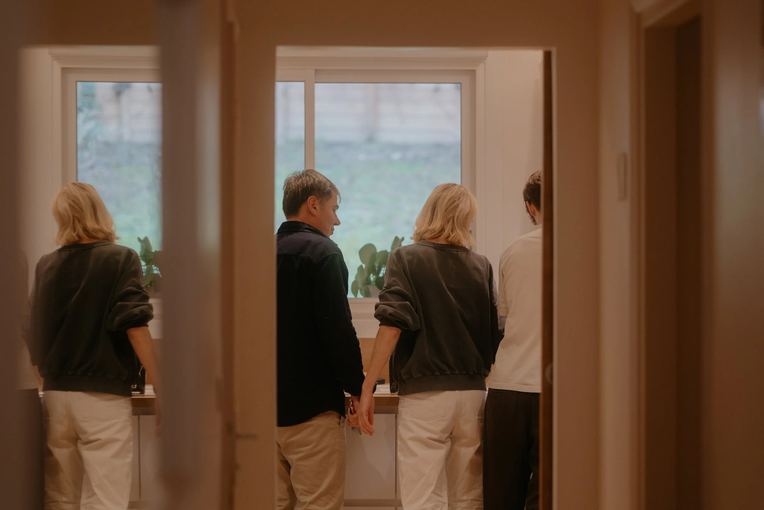 Une famille debout en cuisine, yeux baissés, dans une pièce avec fenêtre, vues de derrière.