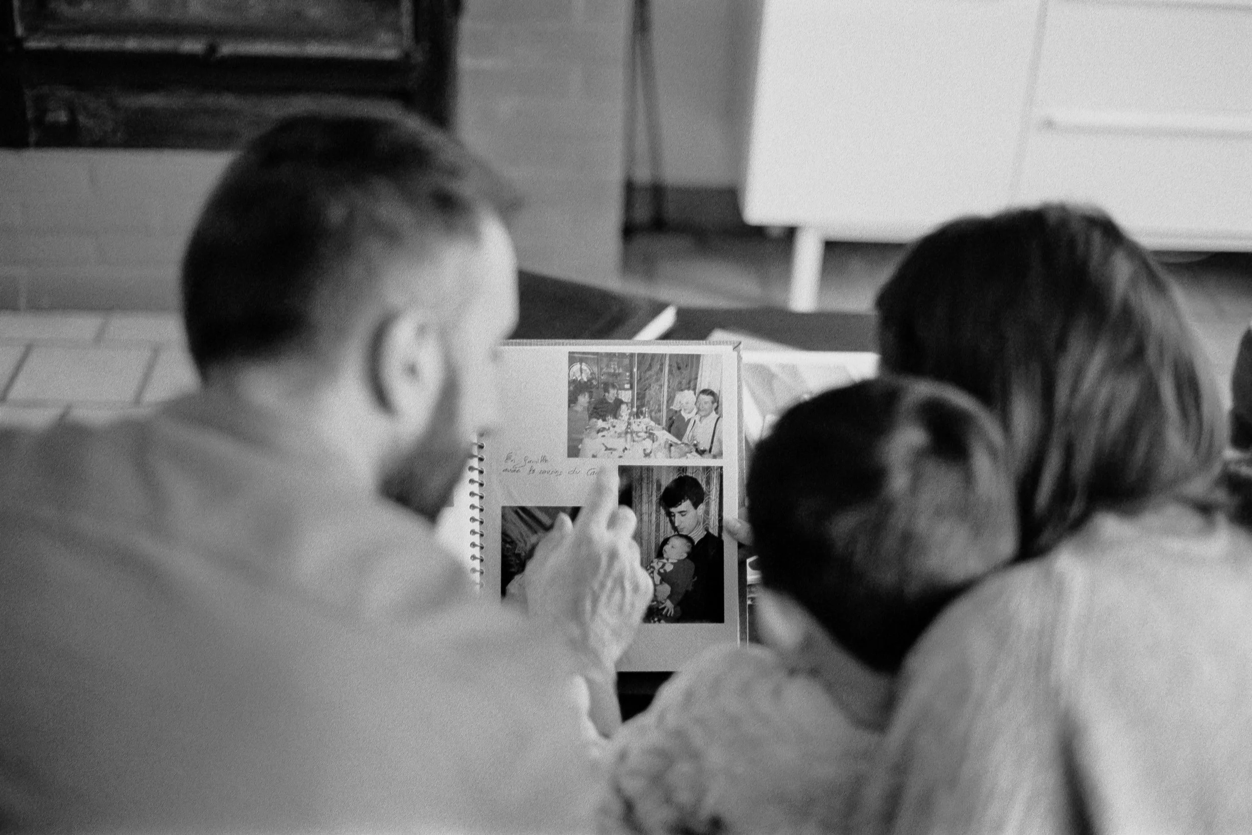 Une famille regarde un album photo de souvenirs d'enfance, assis autour d'une table dans une pièce domestique.