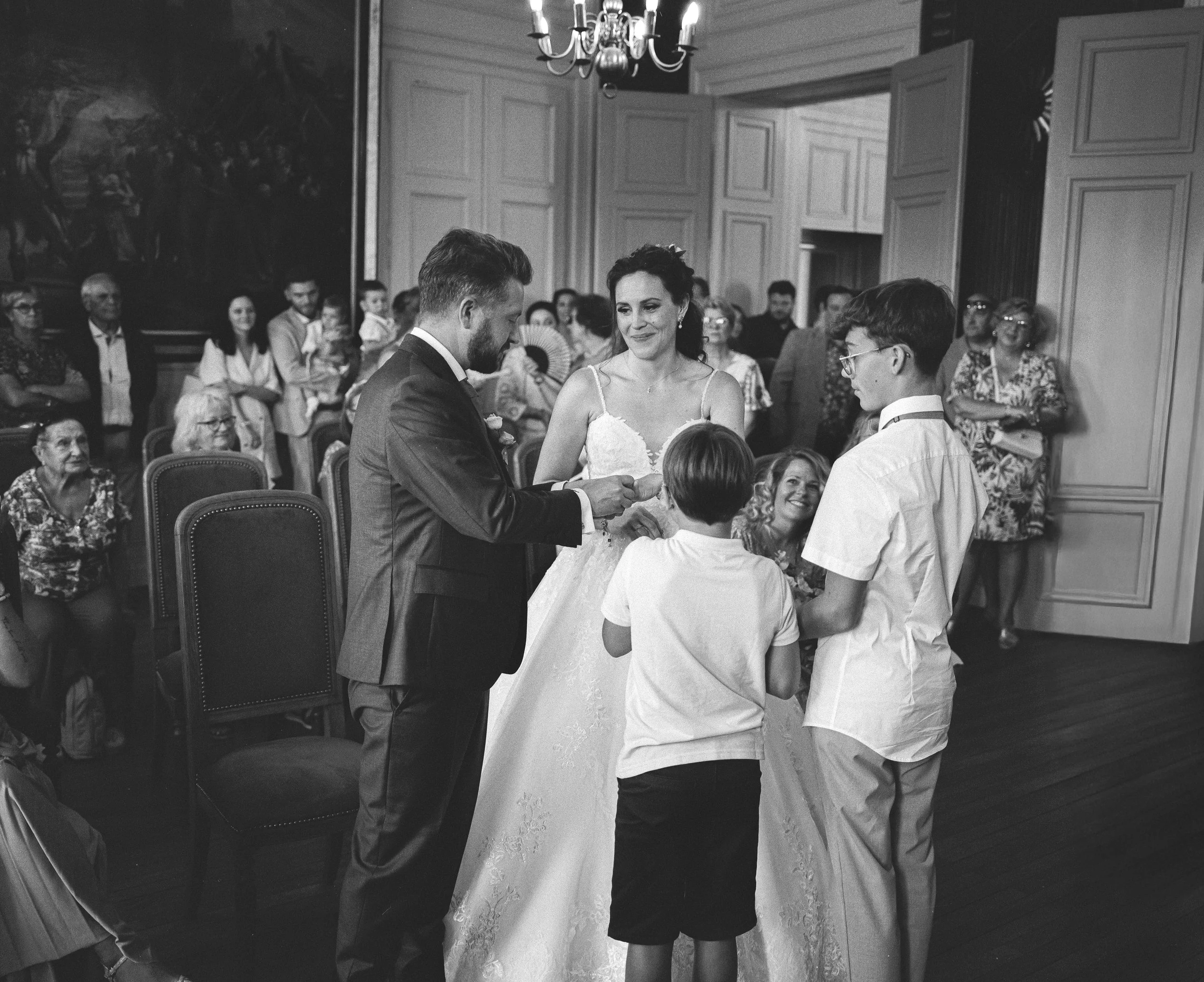 Le marié passe la bague au doigt de la mariée devant leurs invités à la mairie. La photo est en noir et blanc avec beaucoup de grain pour un aspect ancien et rétro