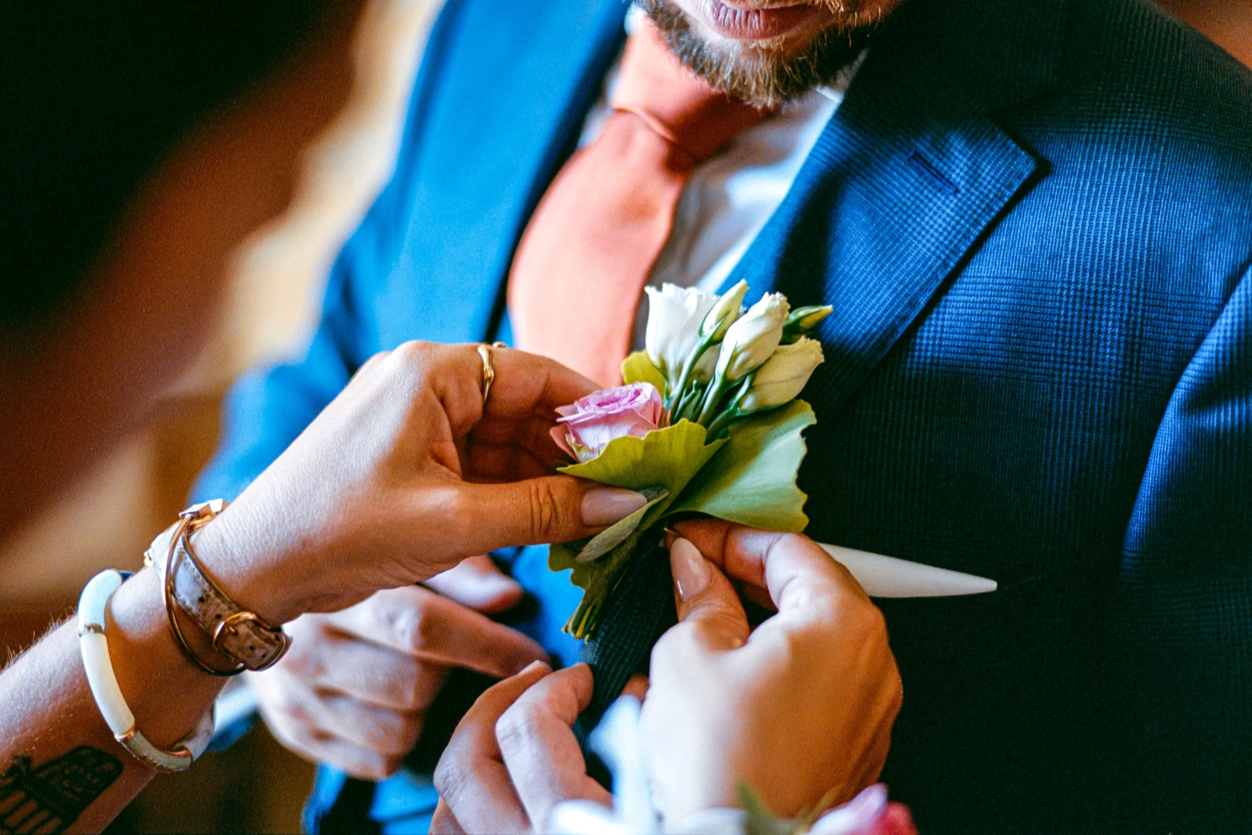 Une personne aide à fixer une boutonnière de fleurs sur la veste d'un homme en costume pour un mariage.