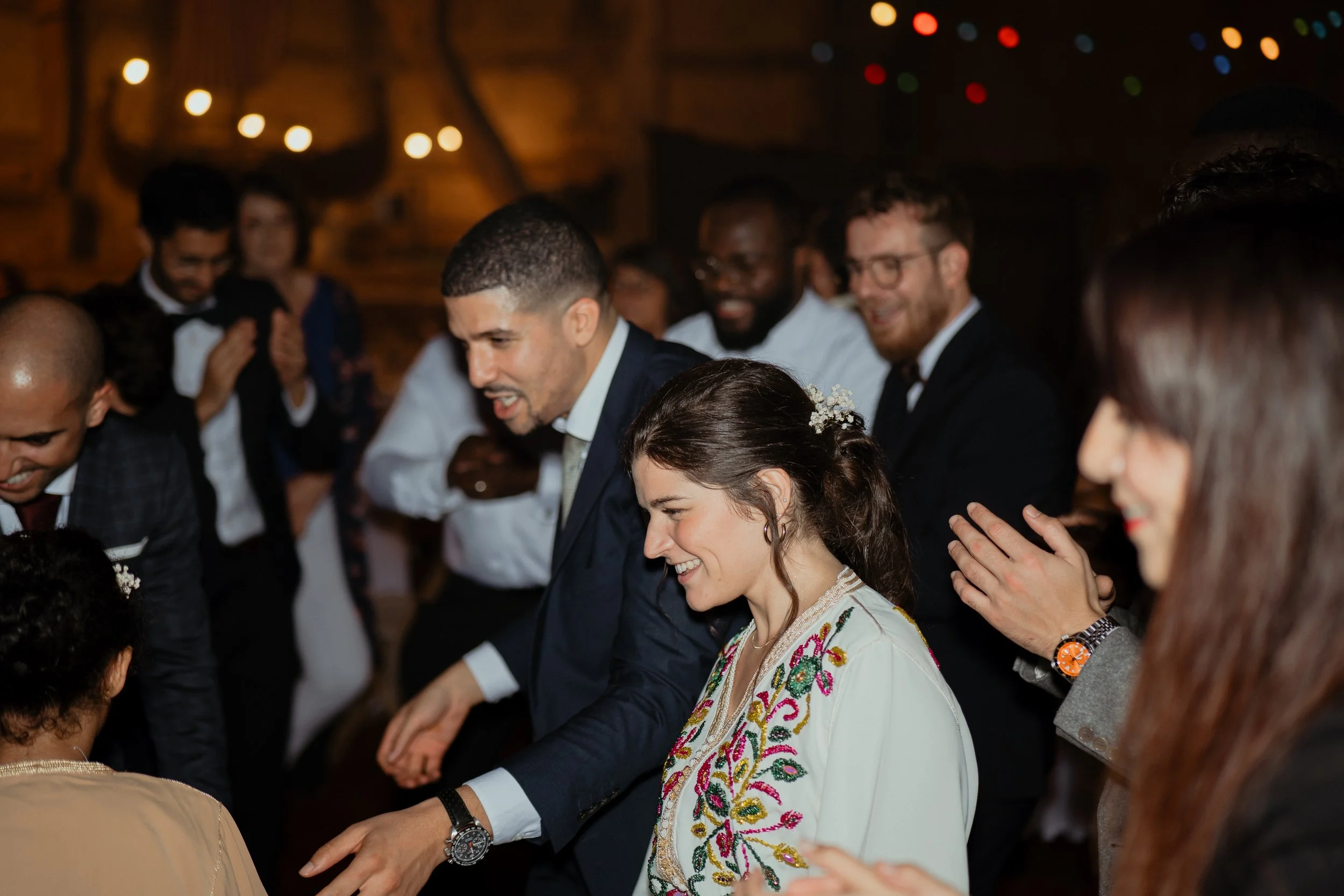 Groupe de personnes lors d'un mariage, applaudissant, dans une ambiance chaleureuse avec des lumières colorées.