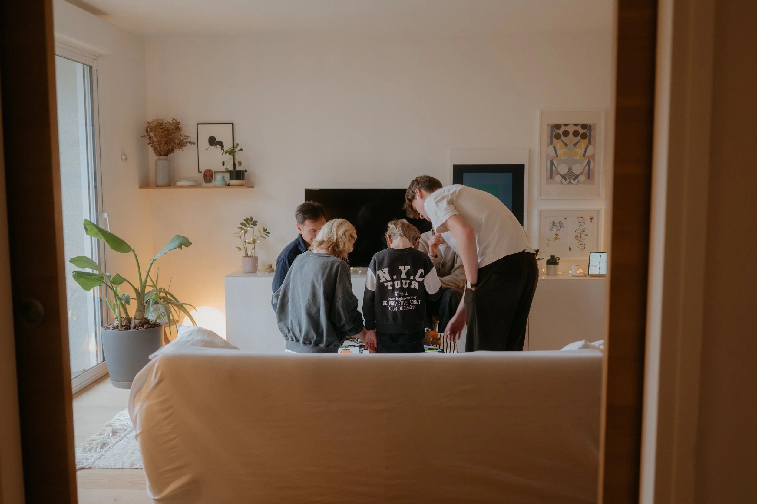 Une famille se rassemble autour d'une table dans un salon moderne et lumineux des Yvelines, en train de faire du dessin ou de faire une activité ensemble, vu depuis l'entrée de la pièce.