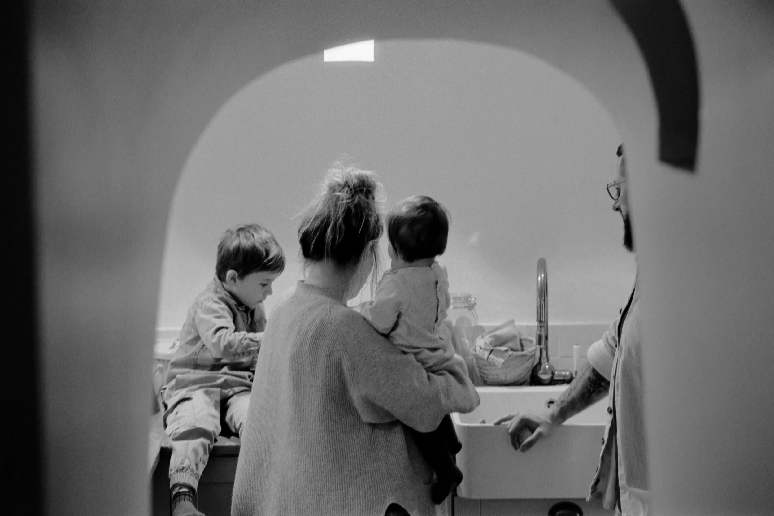 Vue en noir et blanc d'une famille dans une cuisine, vue partielle à travers une ouverture.