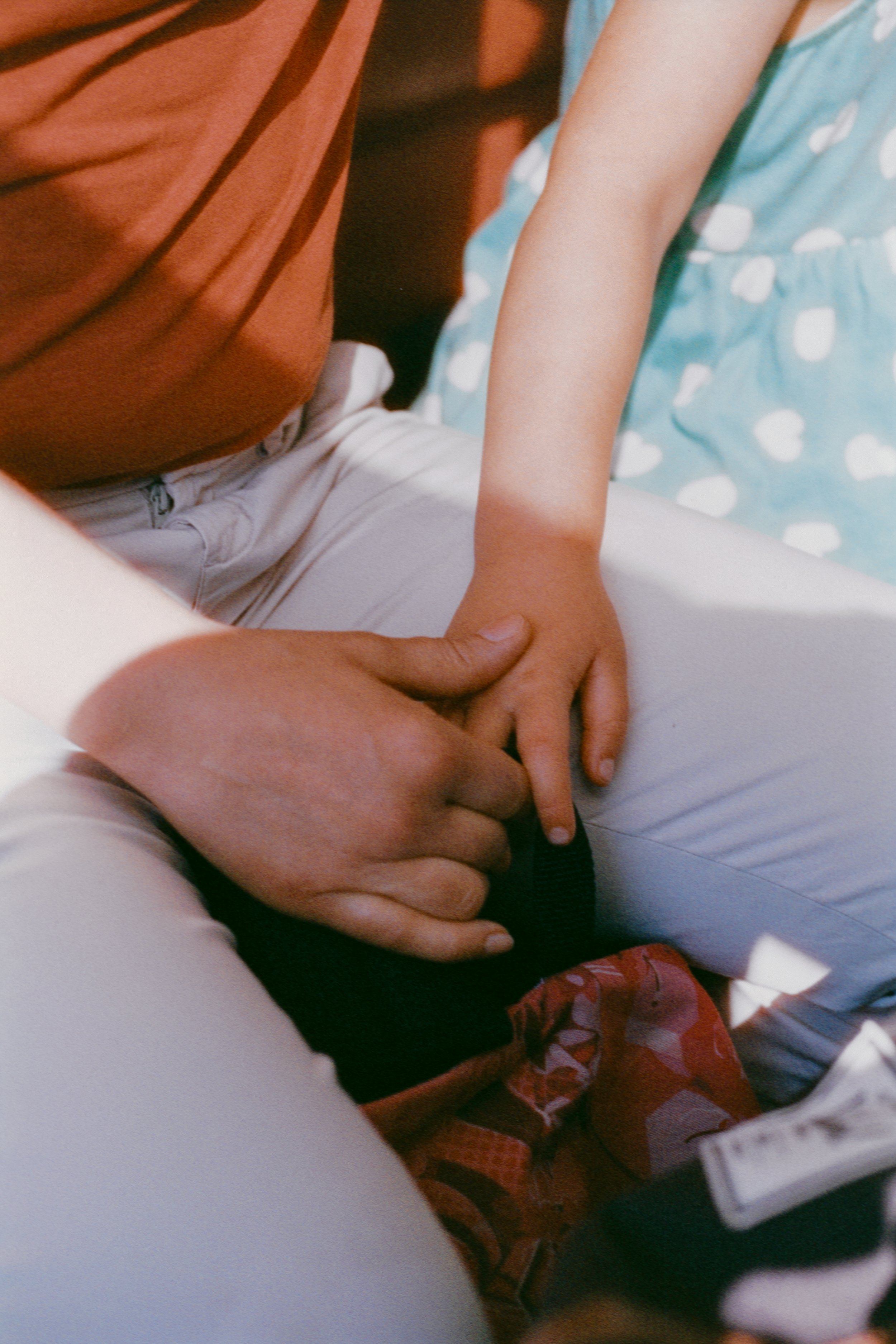 Une mère tenant la main de sa fille, cette dernière porte une robe bleue à pois blancs. Le tout dans une belle lumière chaleureuse.