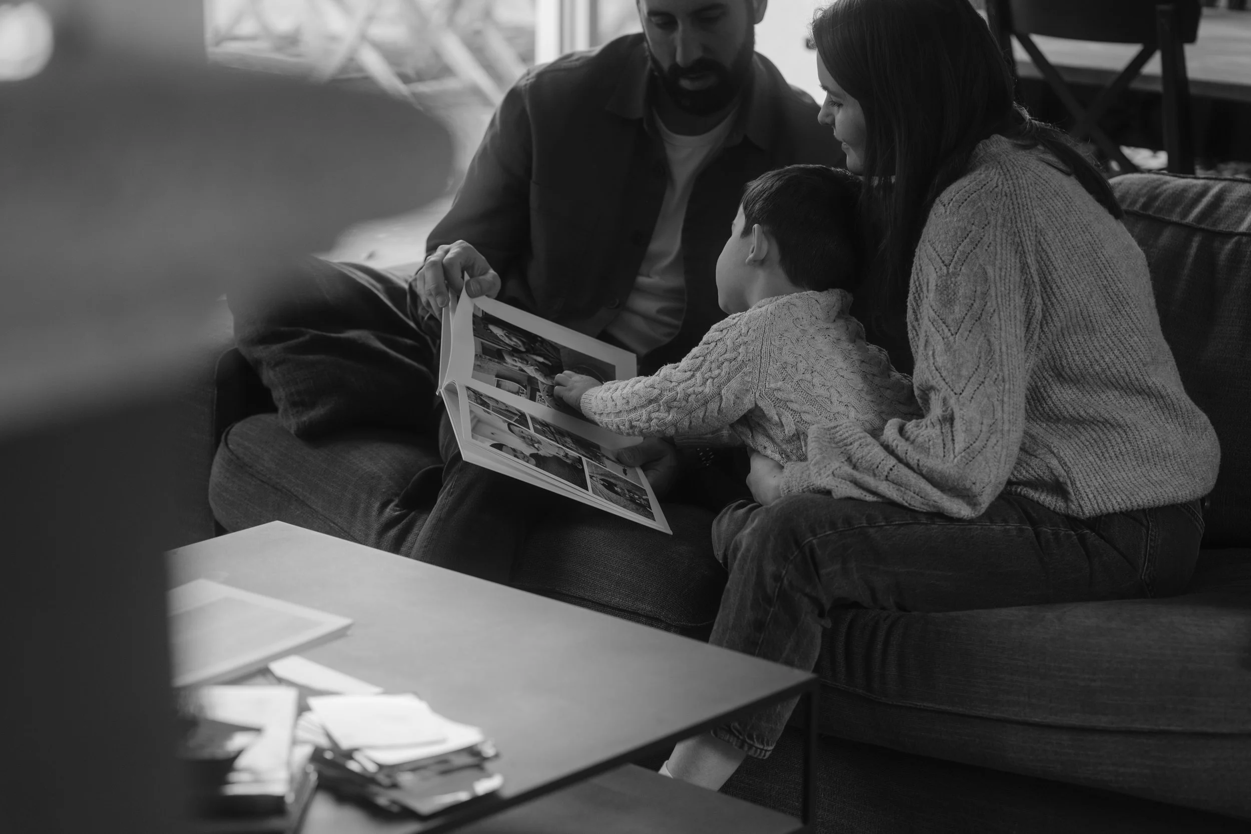 Une famille assise sur un canapé, regardant ensemble un album photo, dans un intérieur domestique des Yvelines.