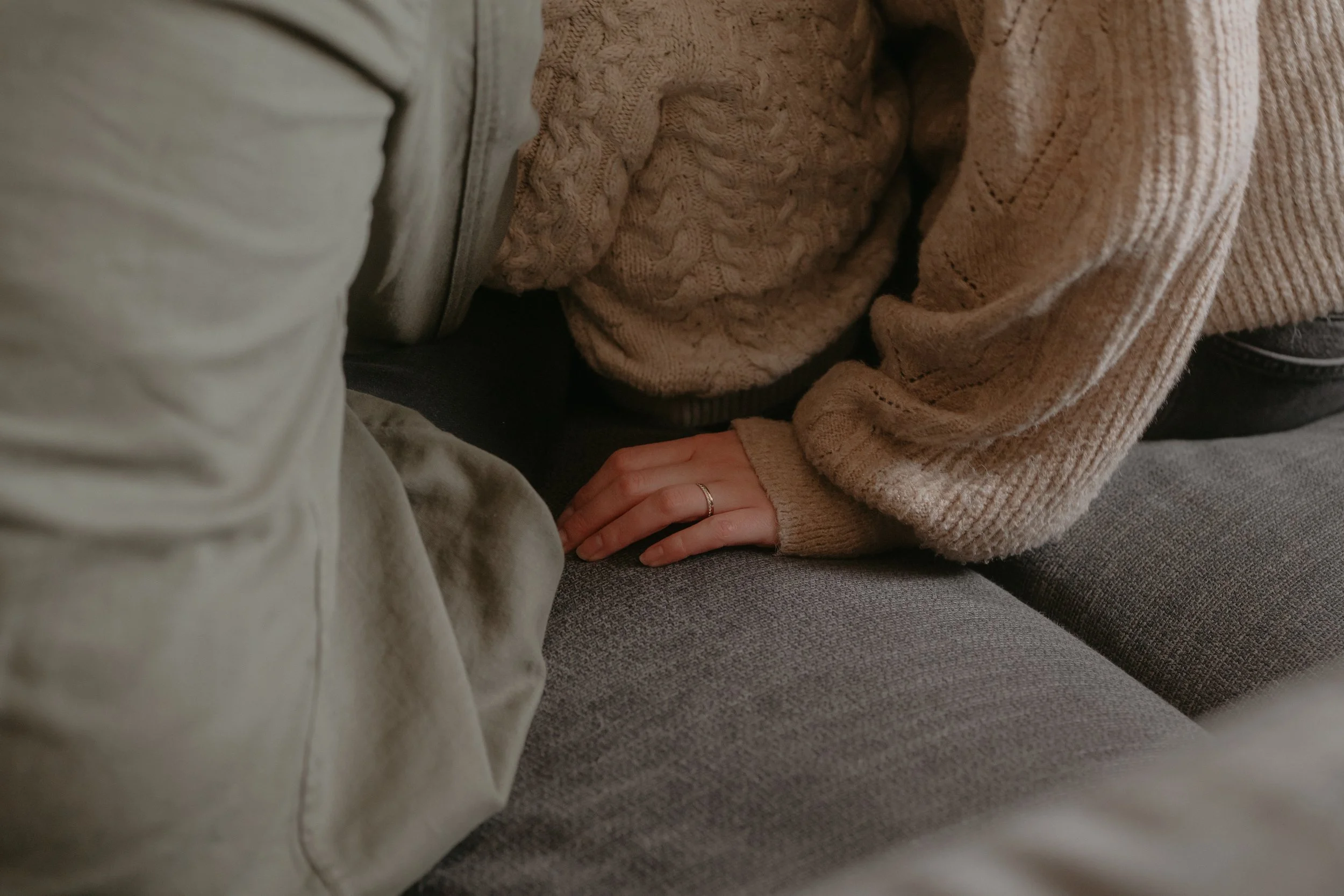 Main d'une maman portant une bague, posées sur le canapé entre deux personnes portant des vêtements en maille beige.