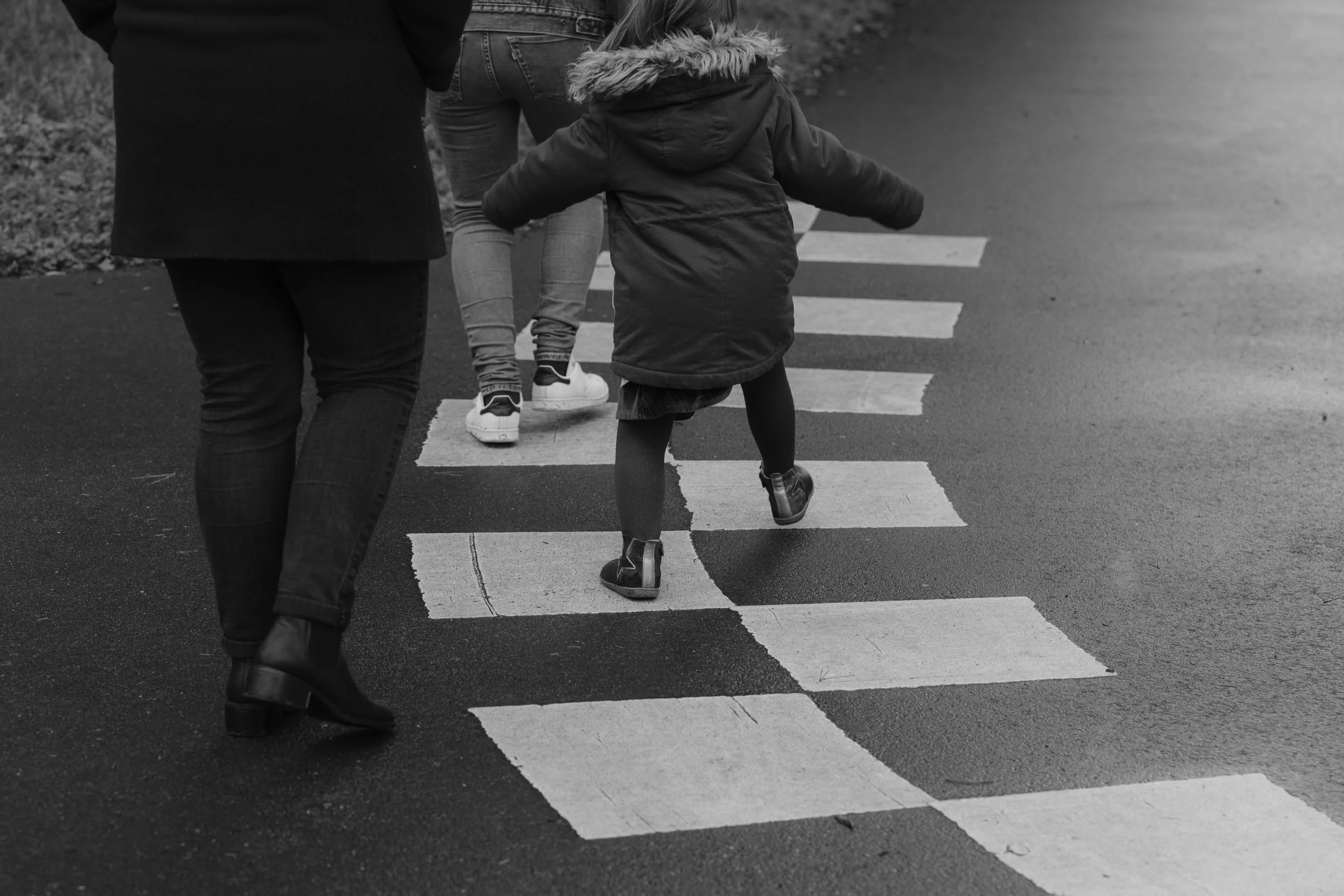 Une enfant marchant sur un passage piéton dans les Yvelines, accompagnée de ses deux parents, en noir et blanc.