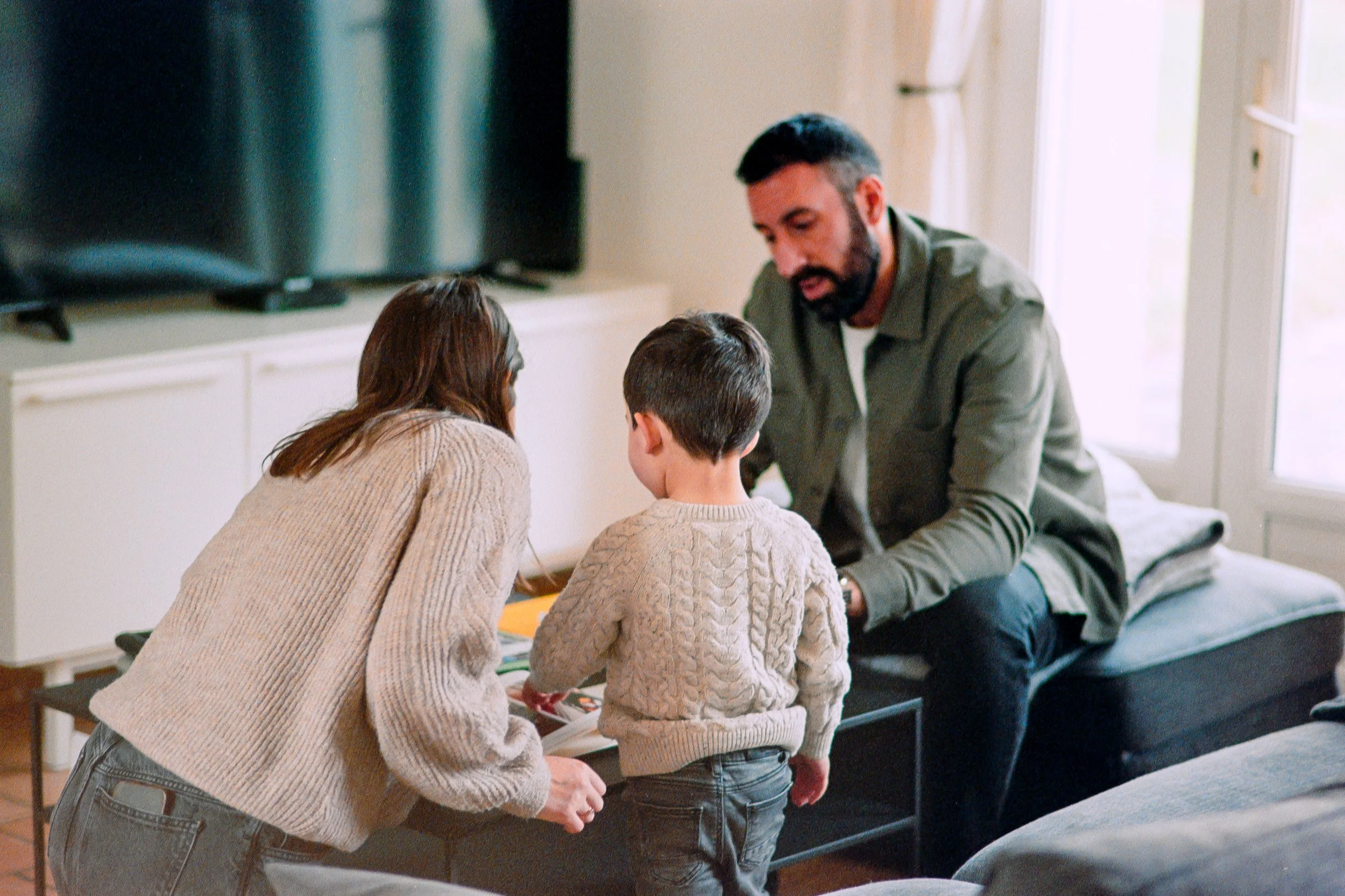 Une famille composée d'un homme, d'une femme et d'un garçon, en train de parler et regarder des photos de famille dans un salon lumineux des Yvelines.