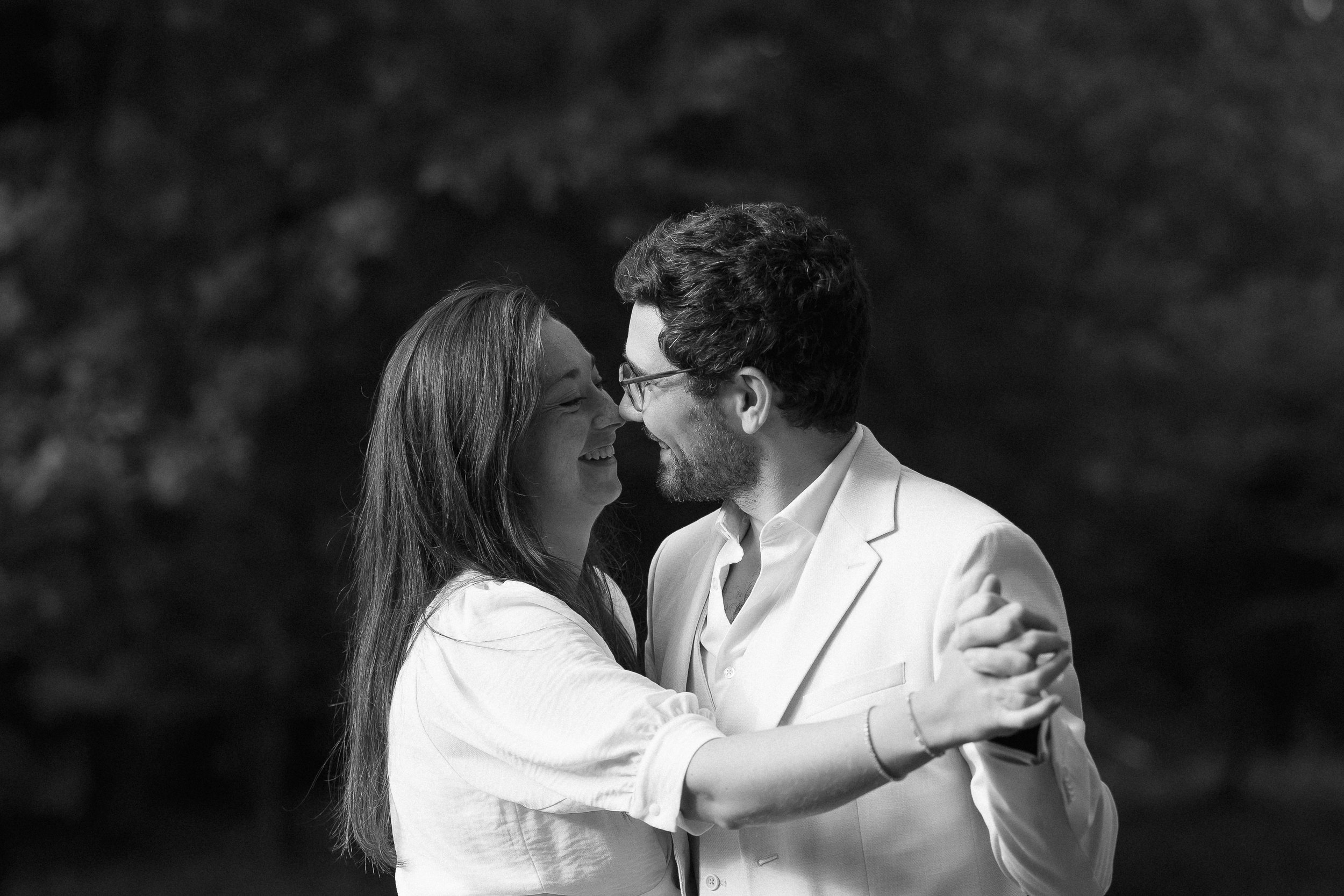 Un couple de jeunes mariés souriant, partageant un moment joyeux, dansant à l'extérieur, en noir et blanc.