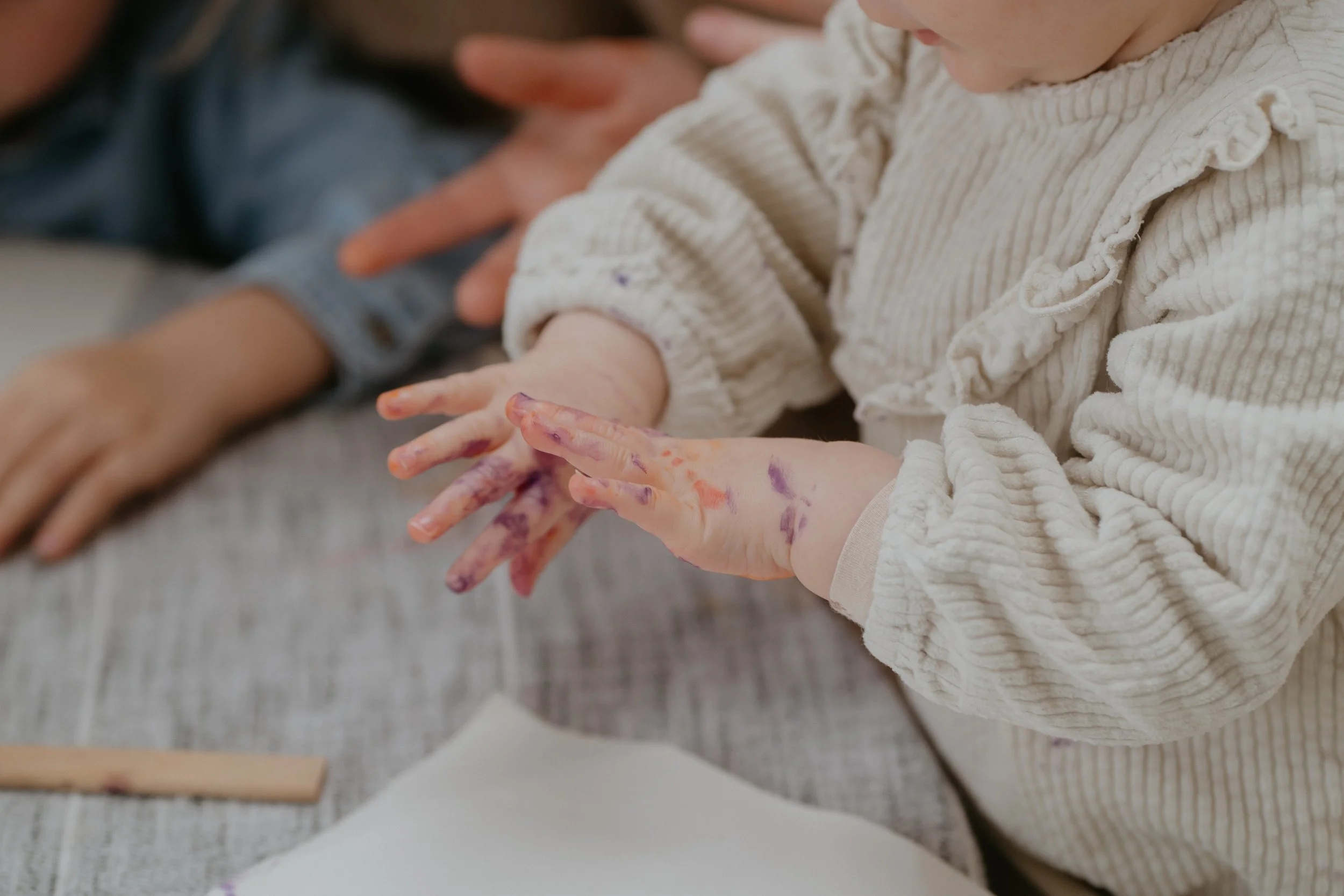 Un enfant avec des mains peintes de différentes couleurs, se concentrant sur une activité artistique. Son frère est partiellement visible à côté.