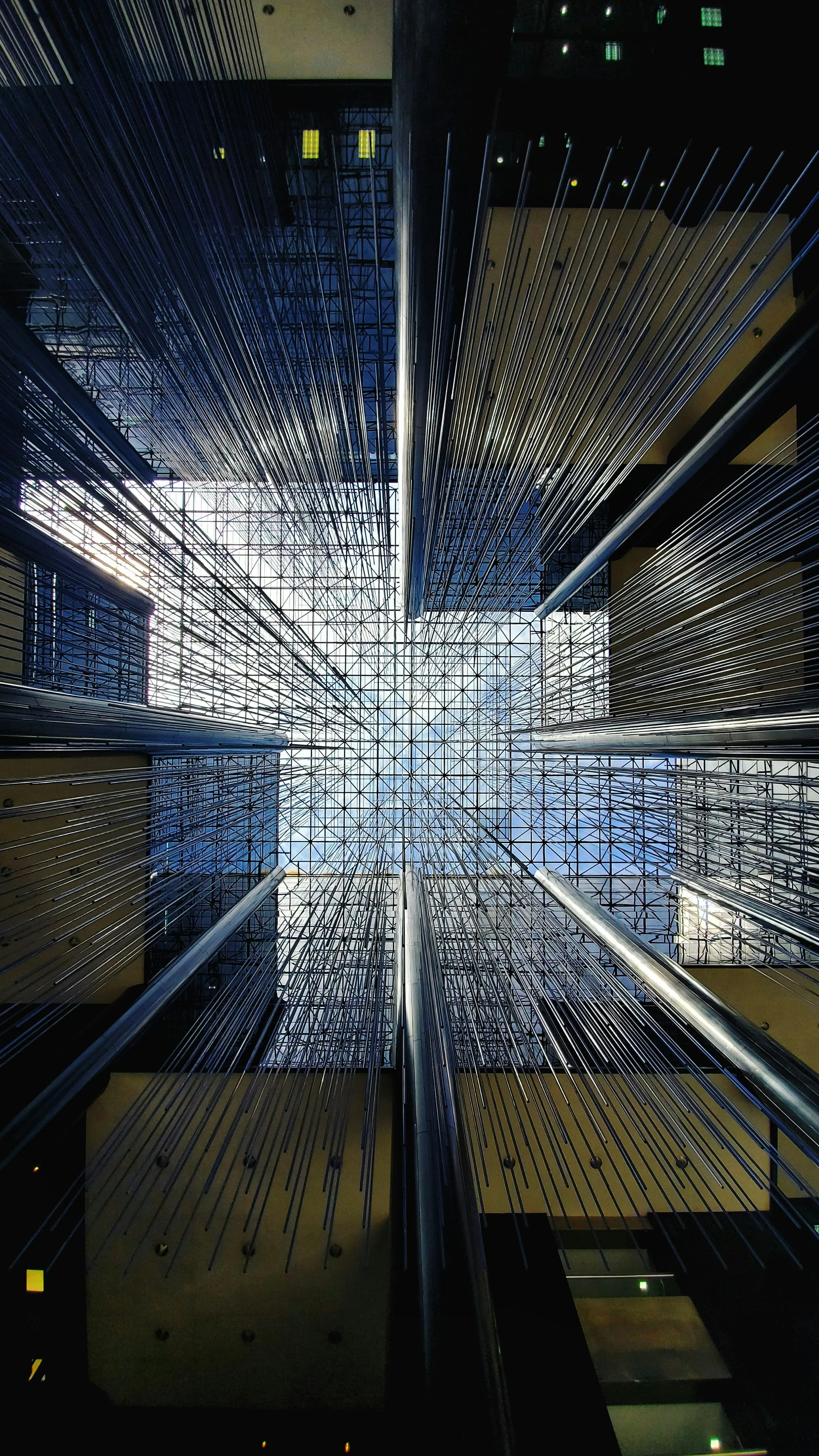 View looking up at a glass atrium ceiling framed by modern high-rise buildings with reflective glass facades, capturing the architectural details from below.