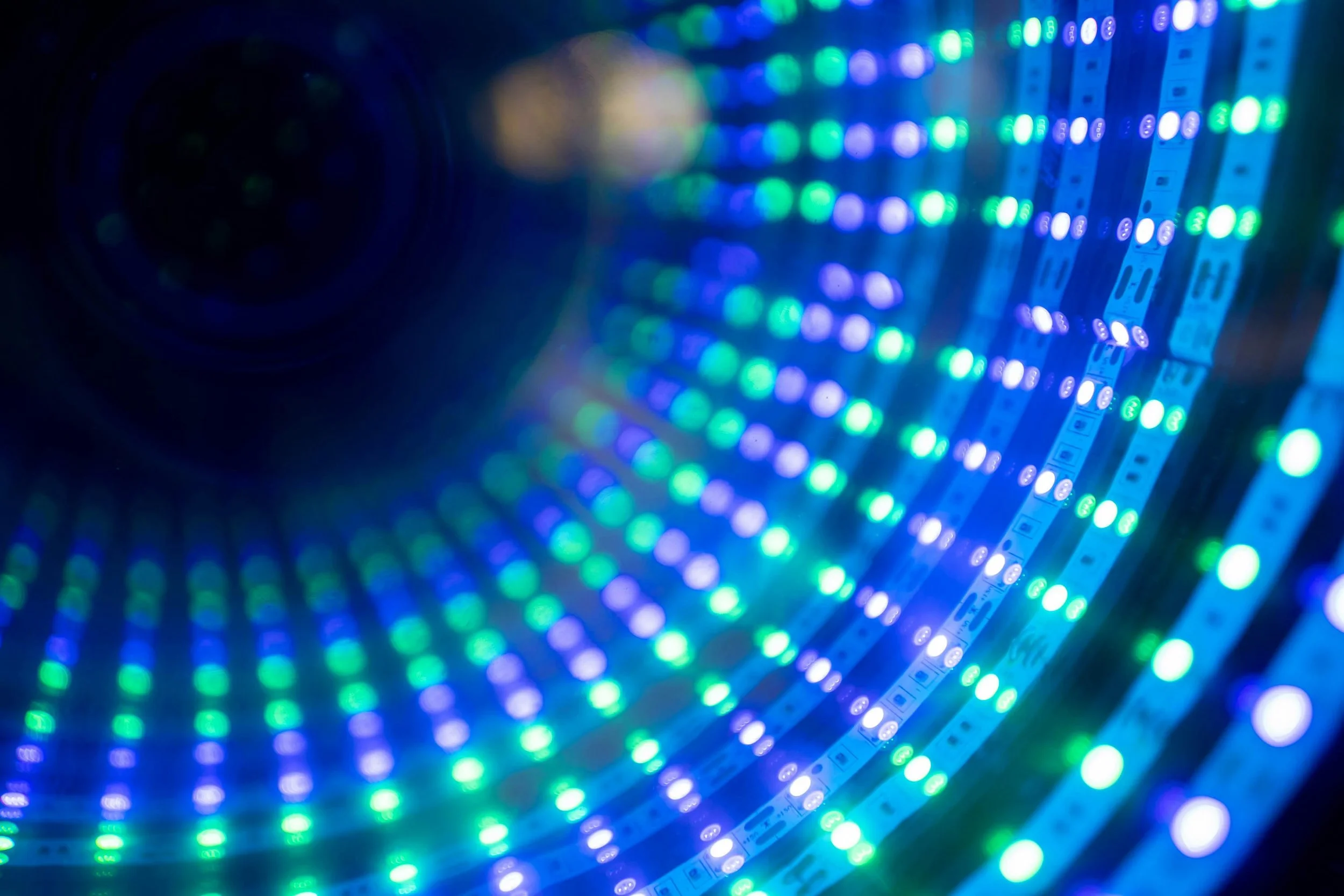 Close-up of a flexible LED light strip emitting blue, green, and purple lights, arranged in a spiral pattern.