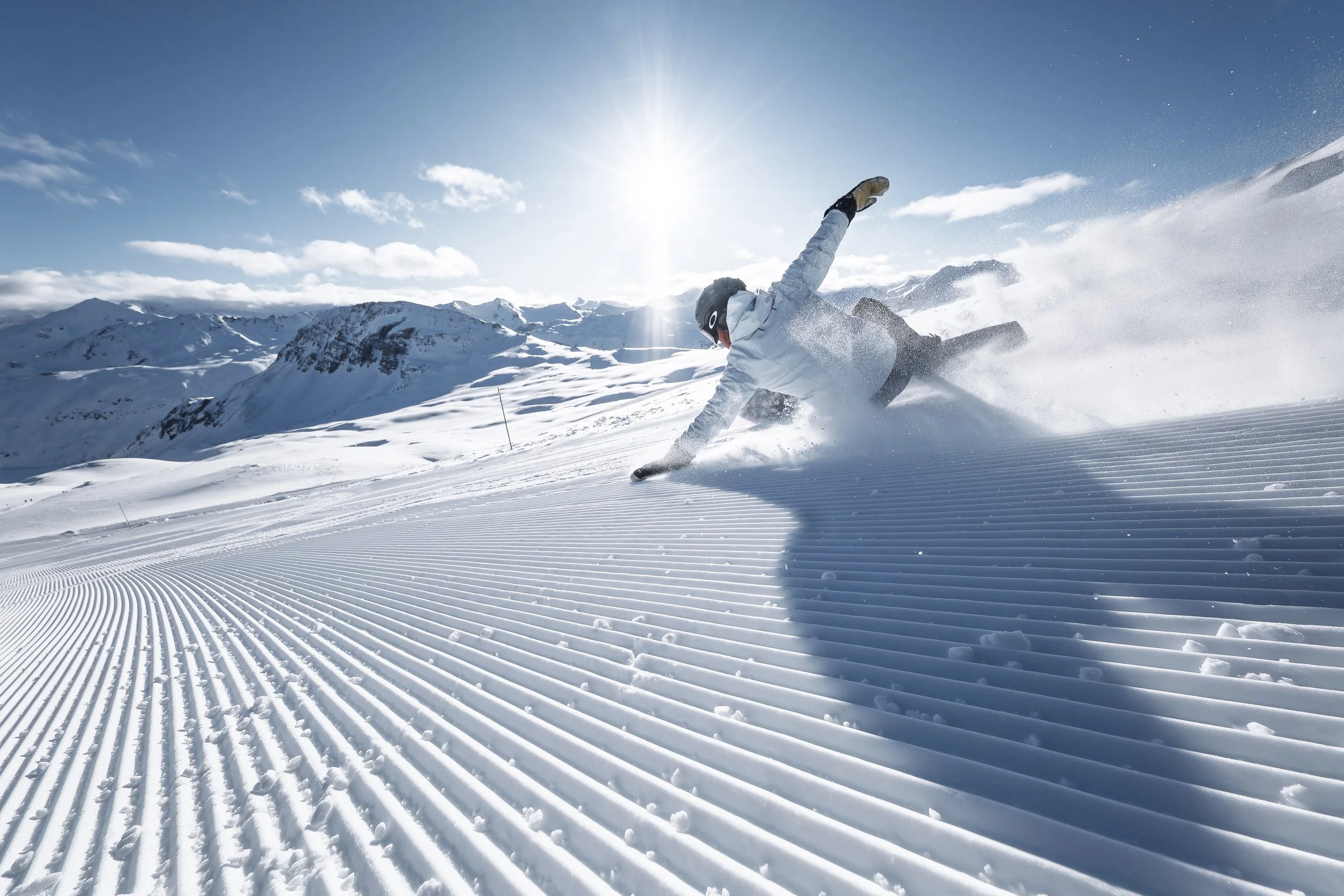 Carving snowboarder heading down a perfectly groomed piste in val d'Isere. White jacket.