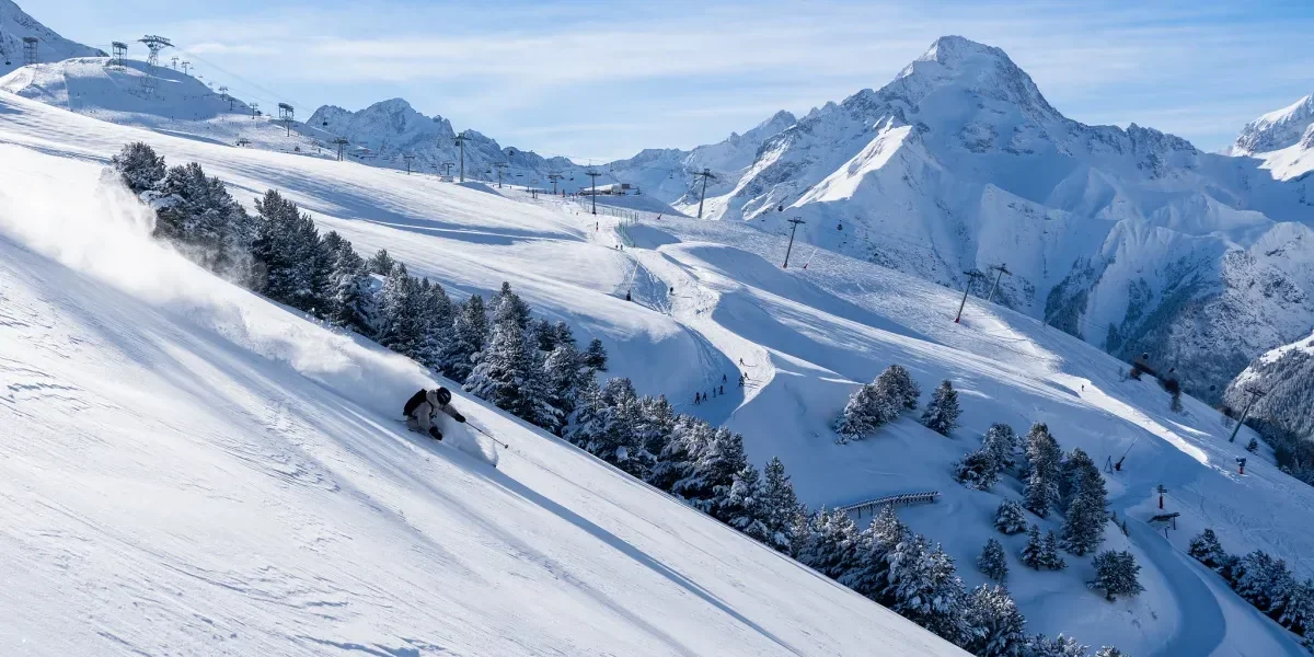 Advanced skier cruising down the mountains with powder dusted trees in the back ground and high mountain peaks.