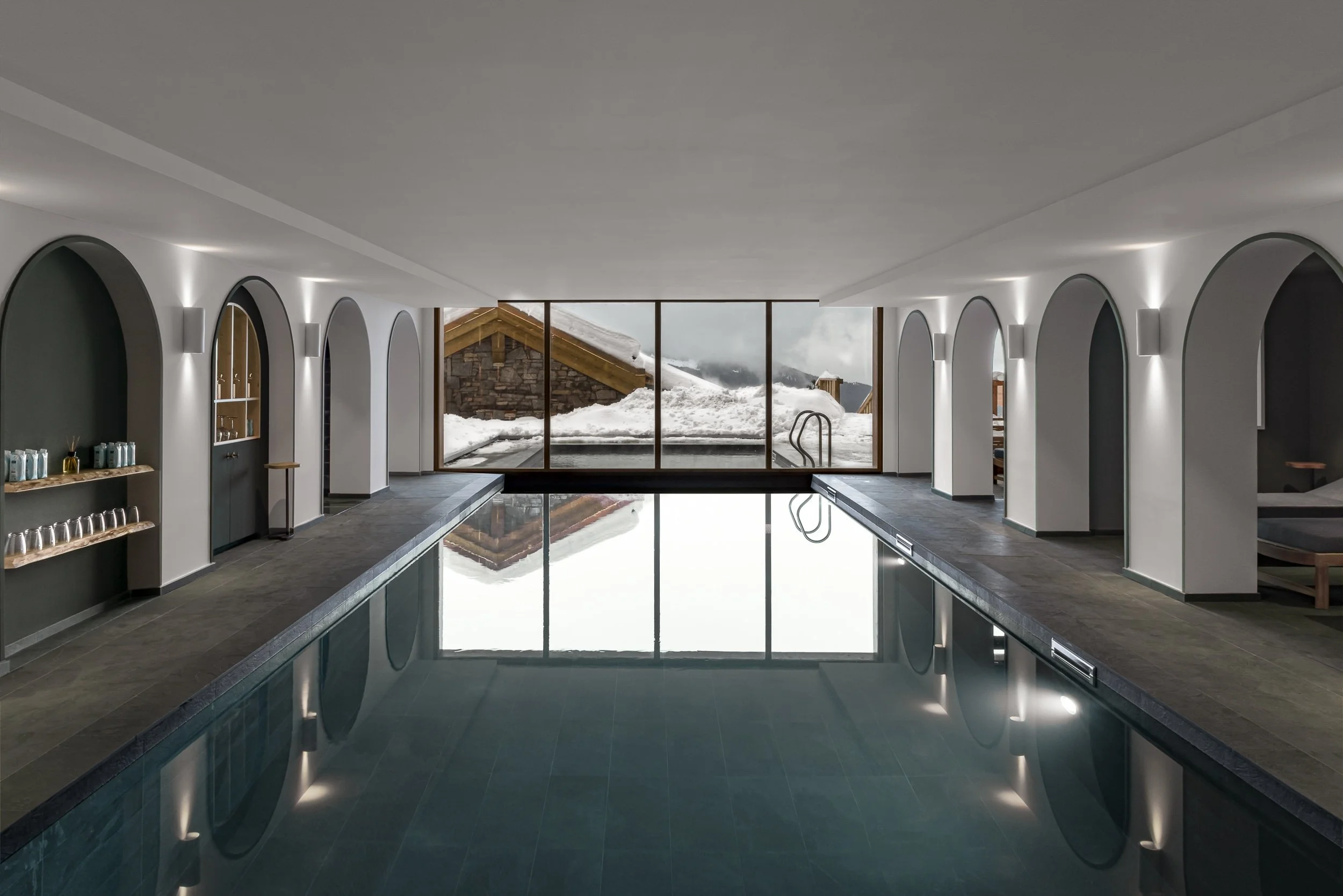 Indoor swimming pool with large windows showing snow-covered mountains outside.