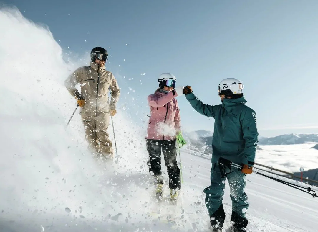 Three alpine skiers who are celebrating a great ski in the sunshine. Fresh snow powdering around and smiles all round.