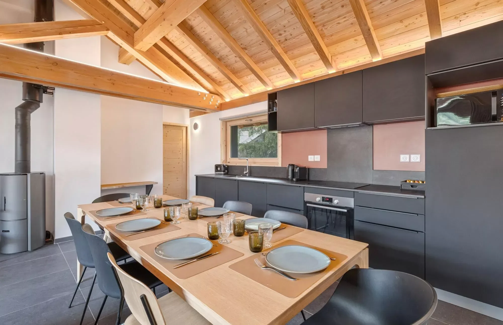 Dining area set for 8 with a modern sleek slate coloured kitchen in the background. Very stylish and modern.