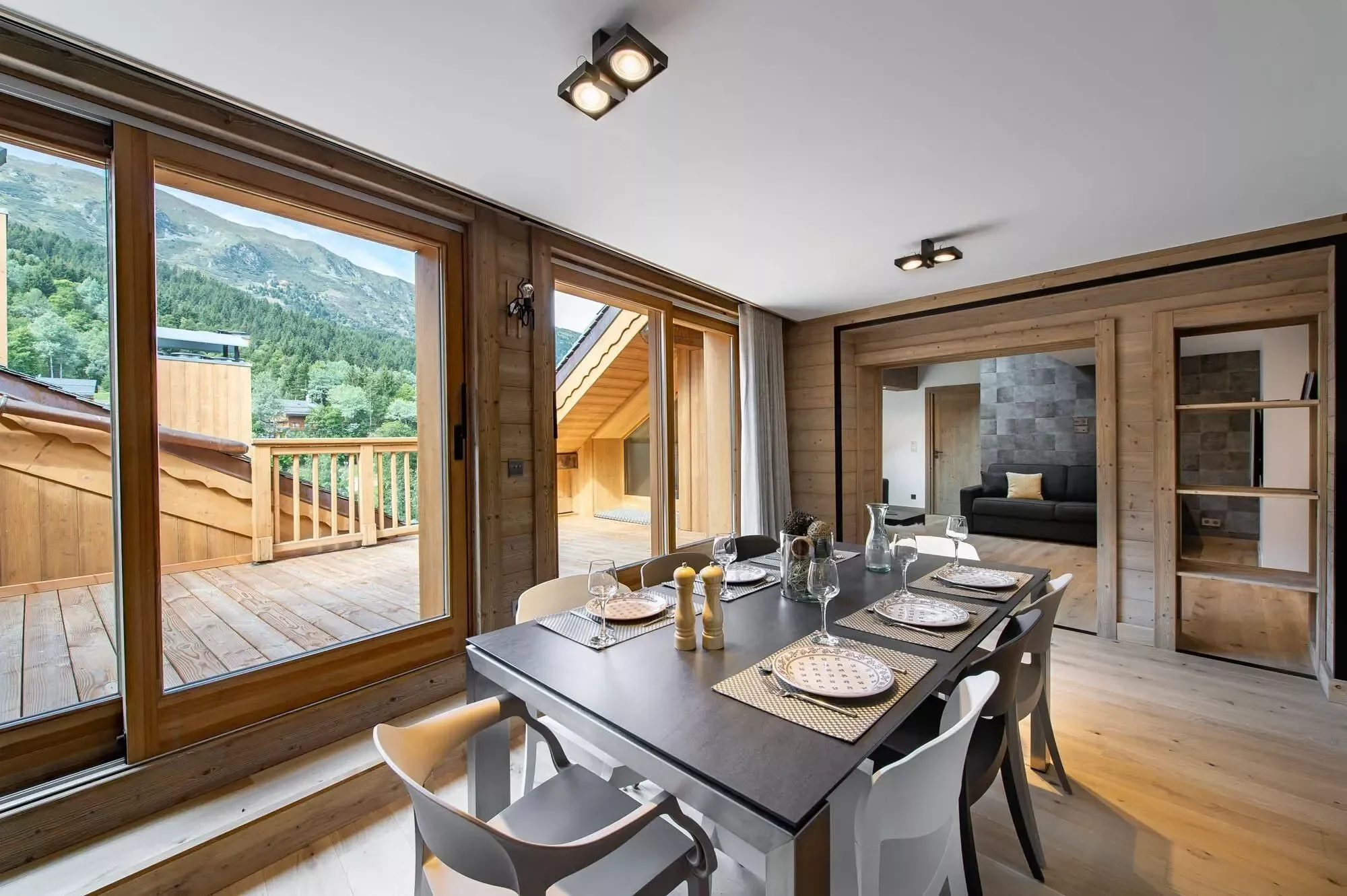 Modern dining table set for six. There is a kitchen in the background and a large terrace. Plenty of natural lighting.