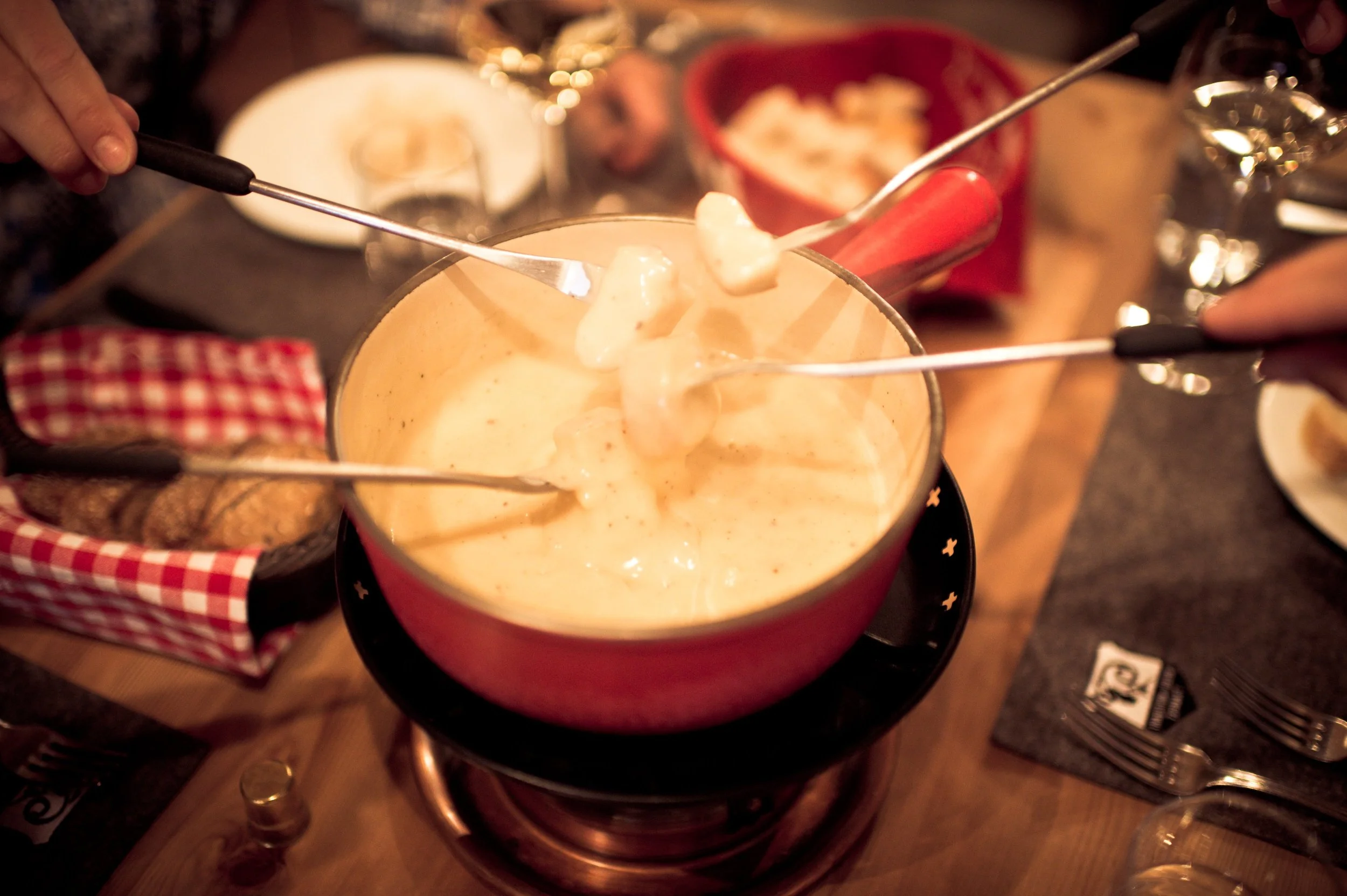 People sharing a cheese fondue with bread and vegetables at a dinner table.
