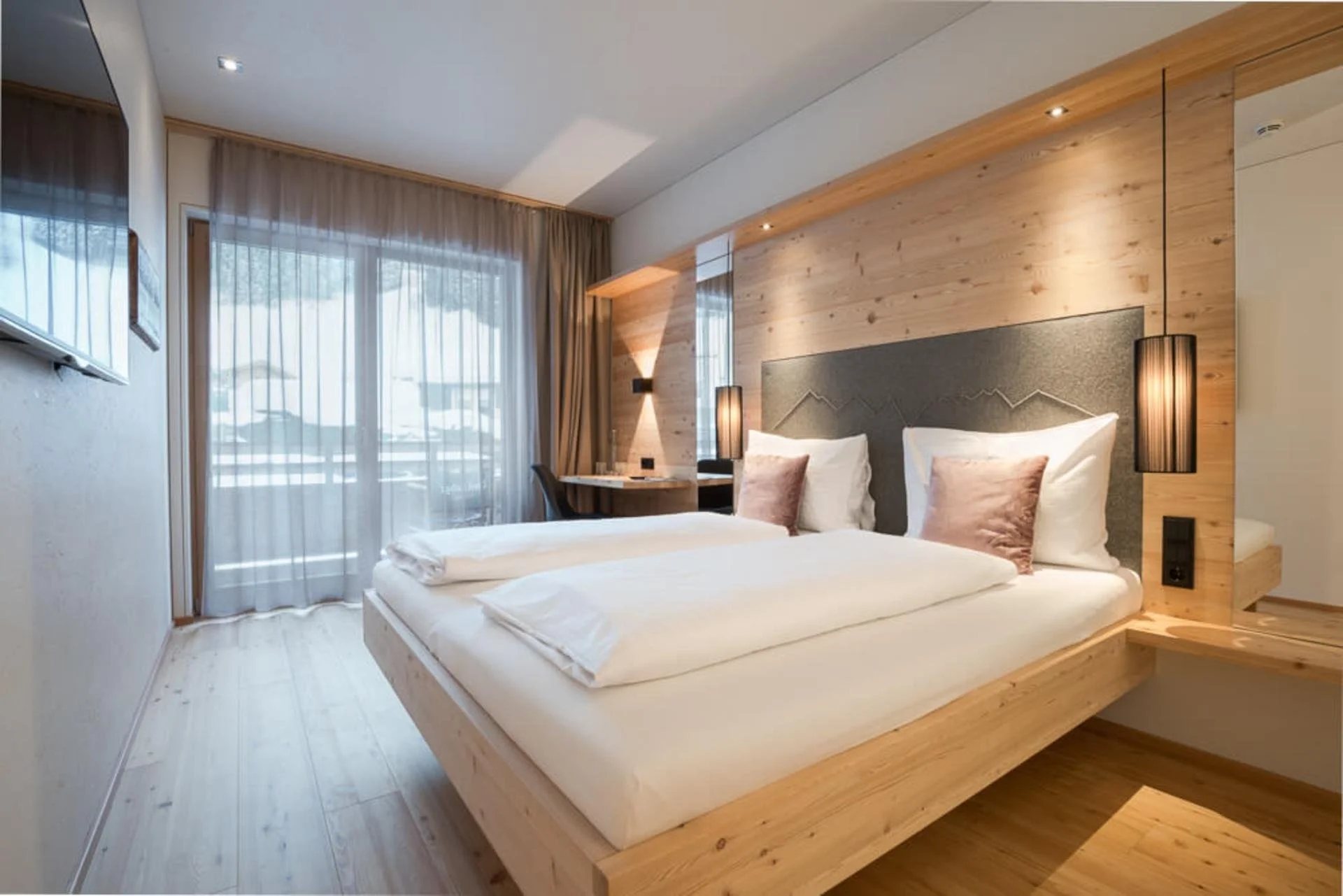 Modern Tirolean style double bed with light pine woods, indulgent bedding and balcony view.