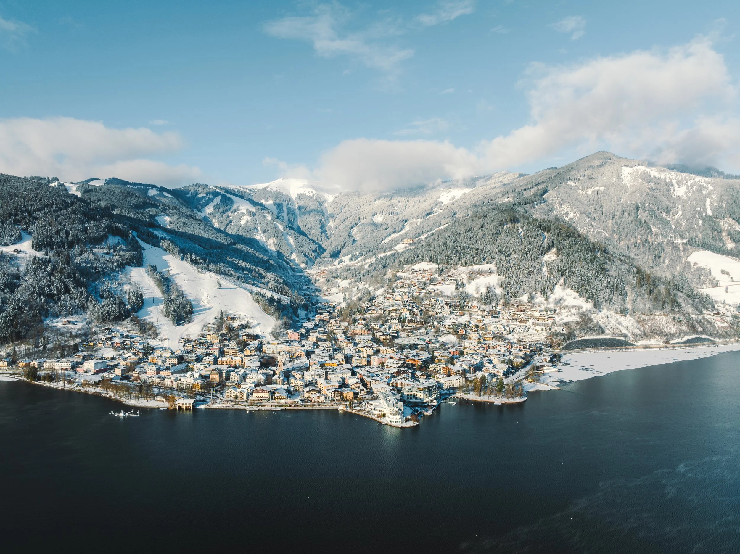 A town located along a lake with snow-covered mountains in the background on a clear winter day.