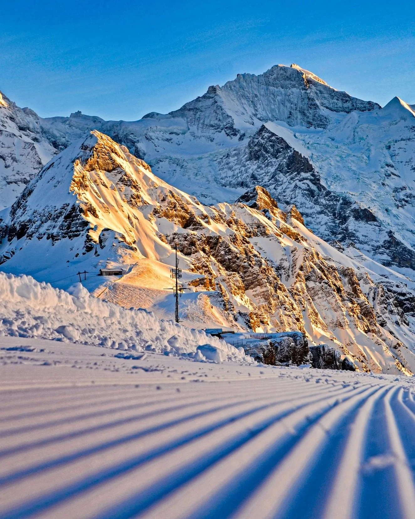 Wengen ski area in the early morning. Here the sun kisses the snowy peaks above freshly groomed pistes.