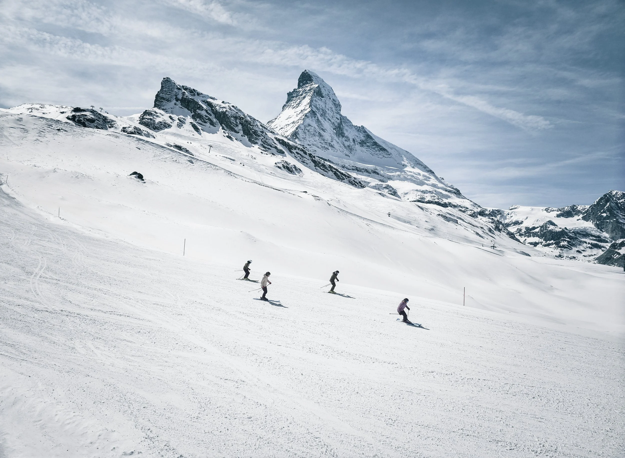 Four friends skiing down a groomed piste in Zermatt, Switzerland in front of the impressive Matterhorn.
