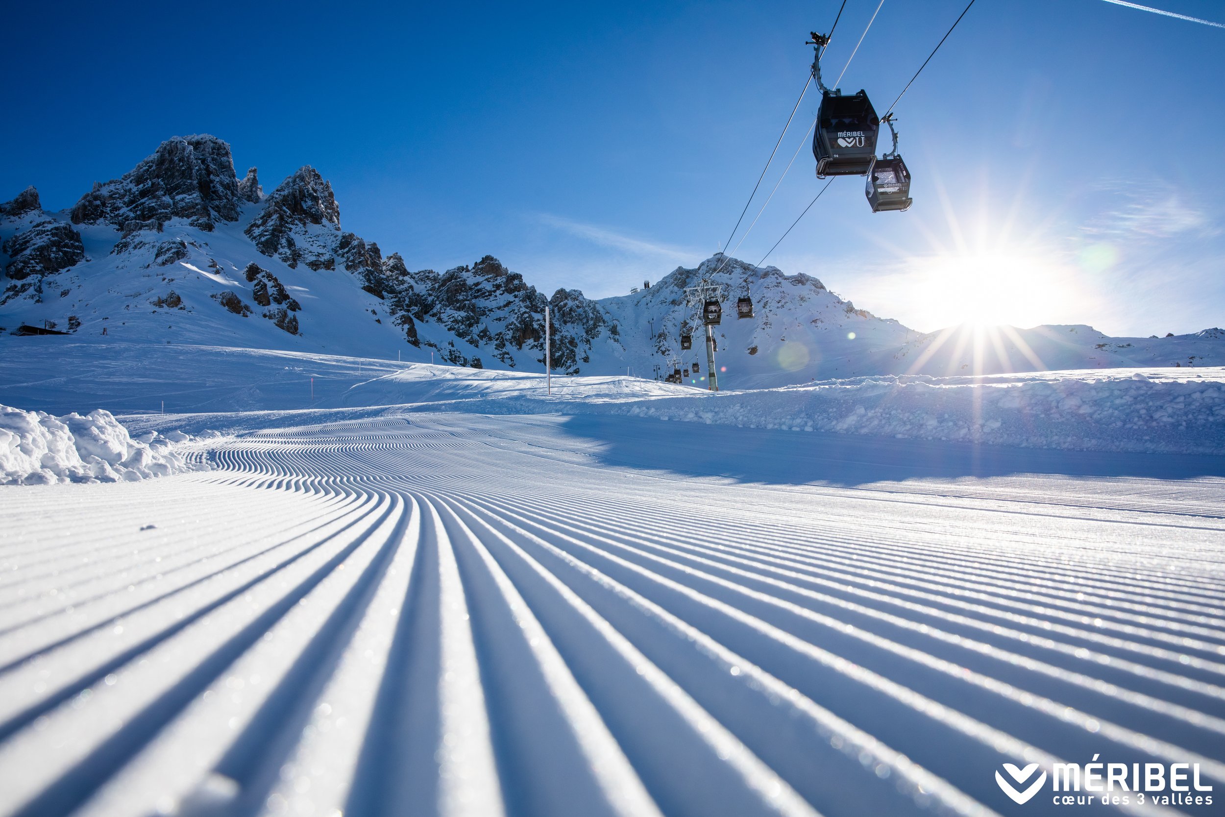 Perfectly groomed piste ready for a fresh day of skiing. Blue skies, cable car overhead and the mountains in the background.