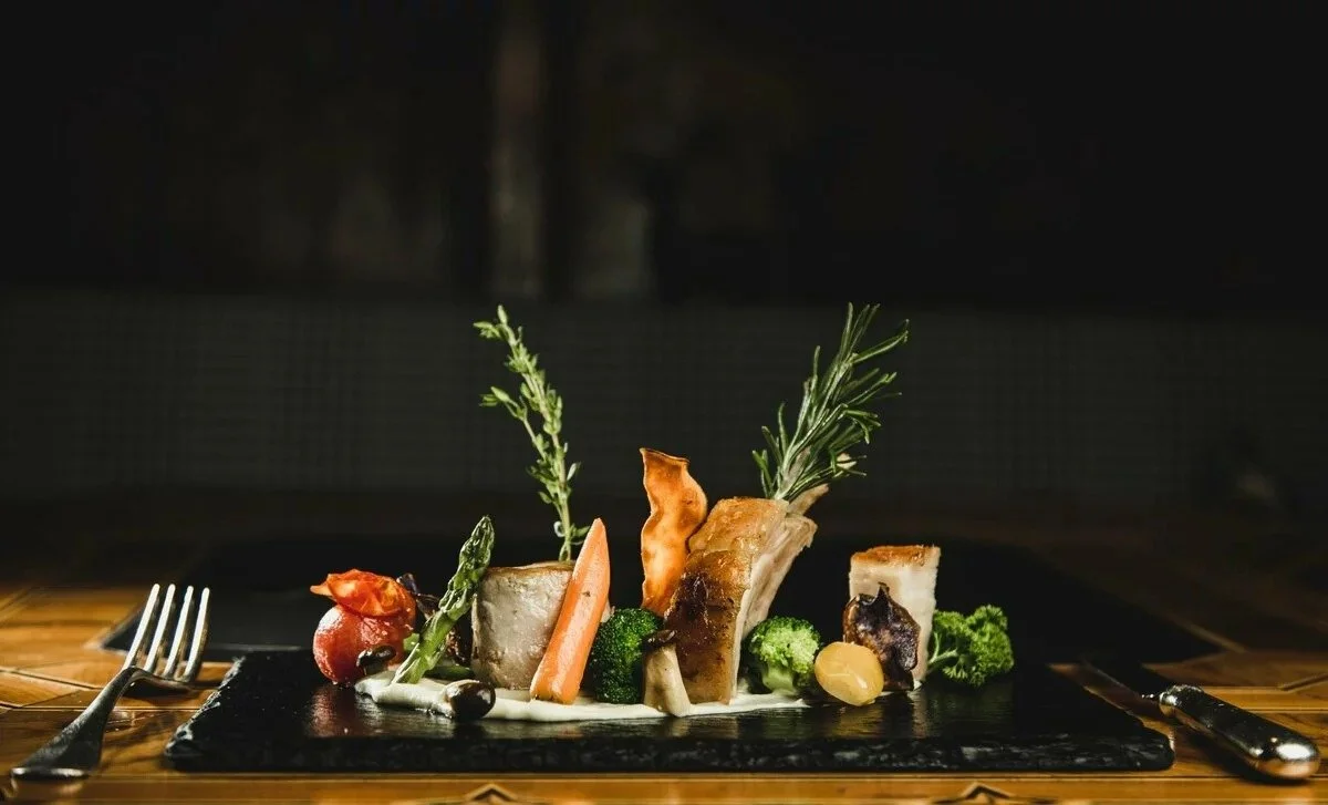 Beautiful contrasting dinnerplate on slate. Pork belly with fresh vegetables sat on a sauce.