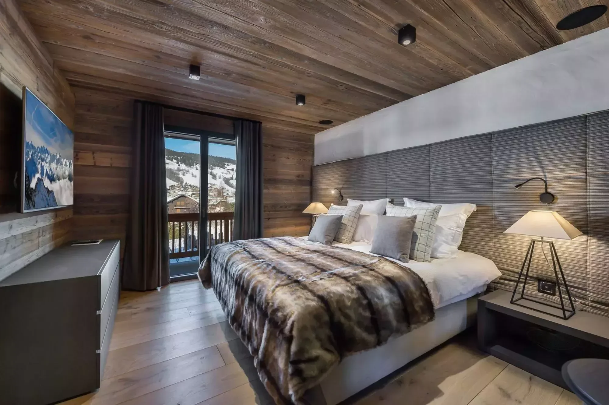 Large double bedroom with wooden flooring and fabric walls create a muted and yet luxurious bedroom. Side table lights and views out to the terrace