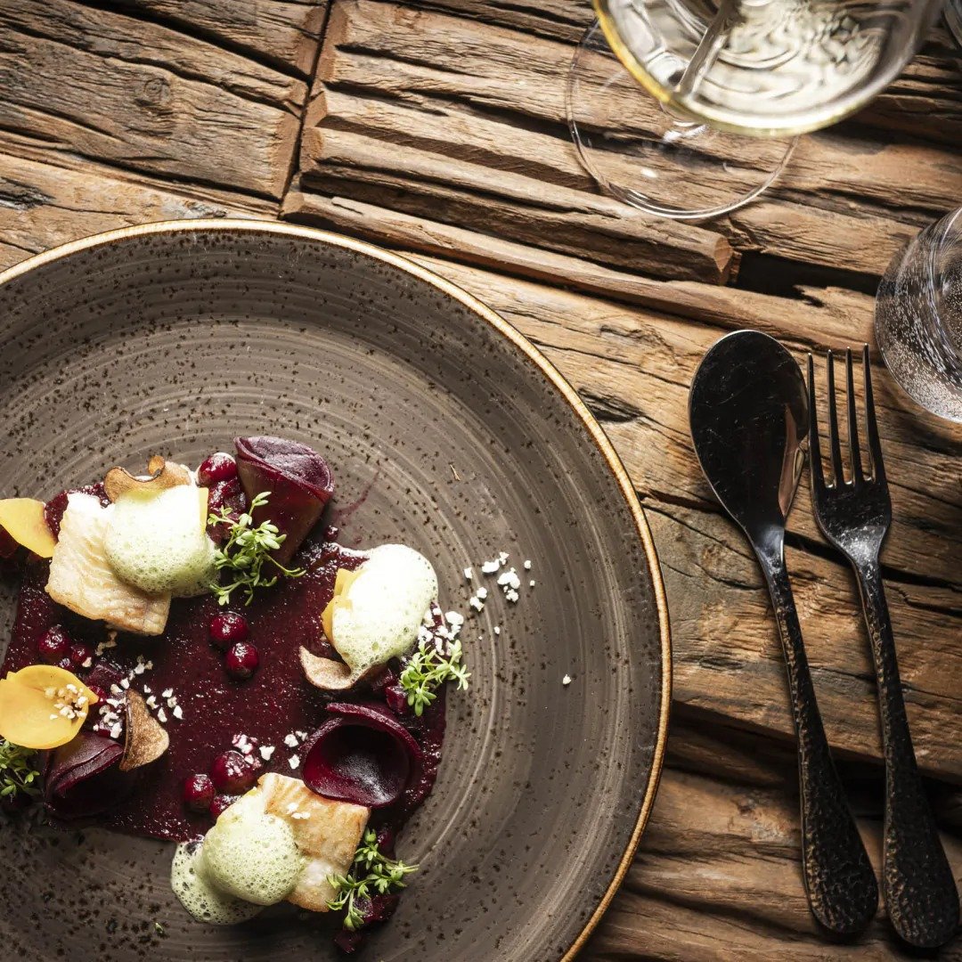 A plate for food which is very colourful and decorative. Beetroots with a beetroot puree, salmon and other wholesome root vegetables