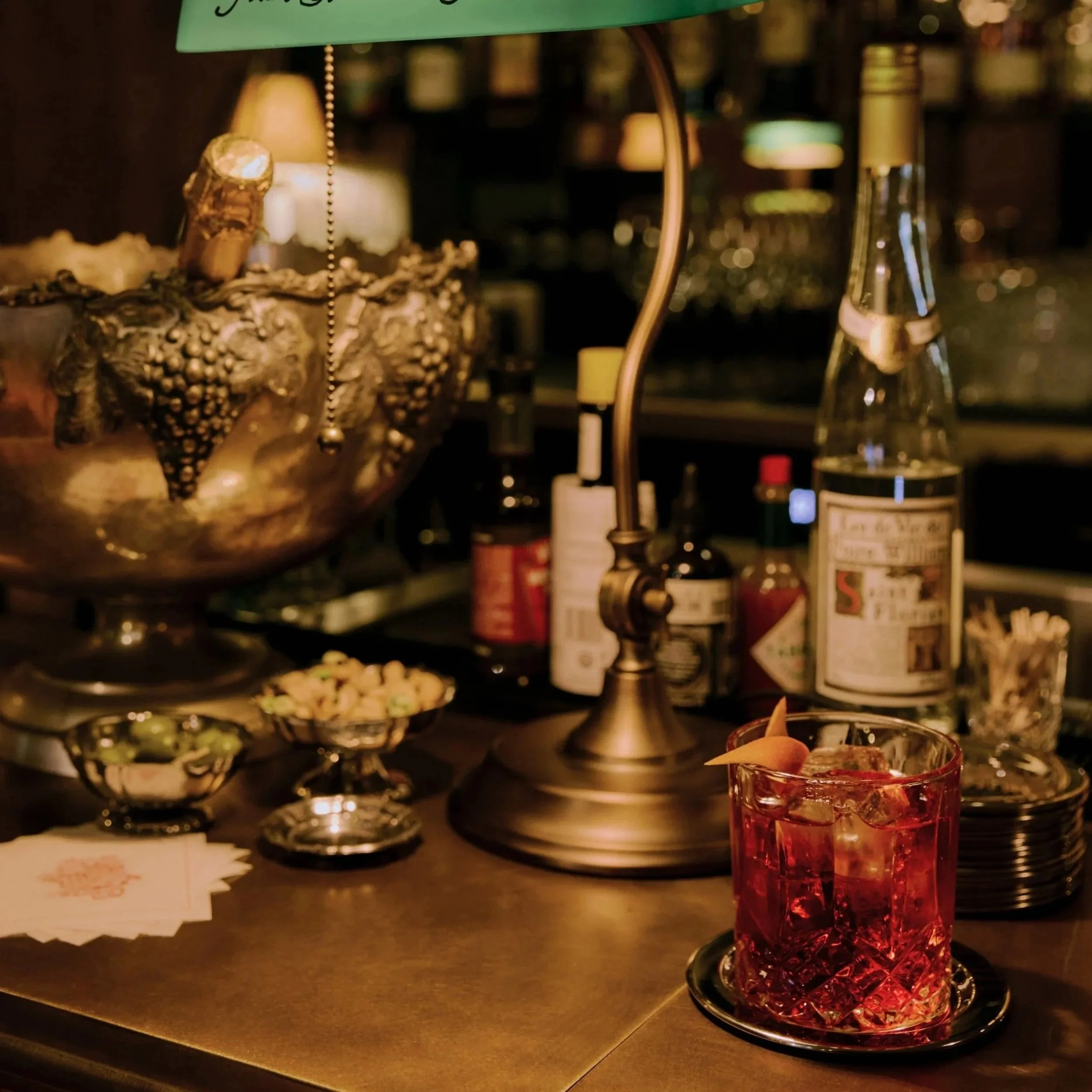 Very plush cosy bar shot with nibbles, Negroni and a classic brass lamp