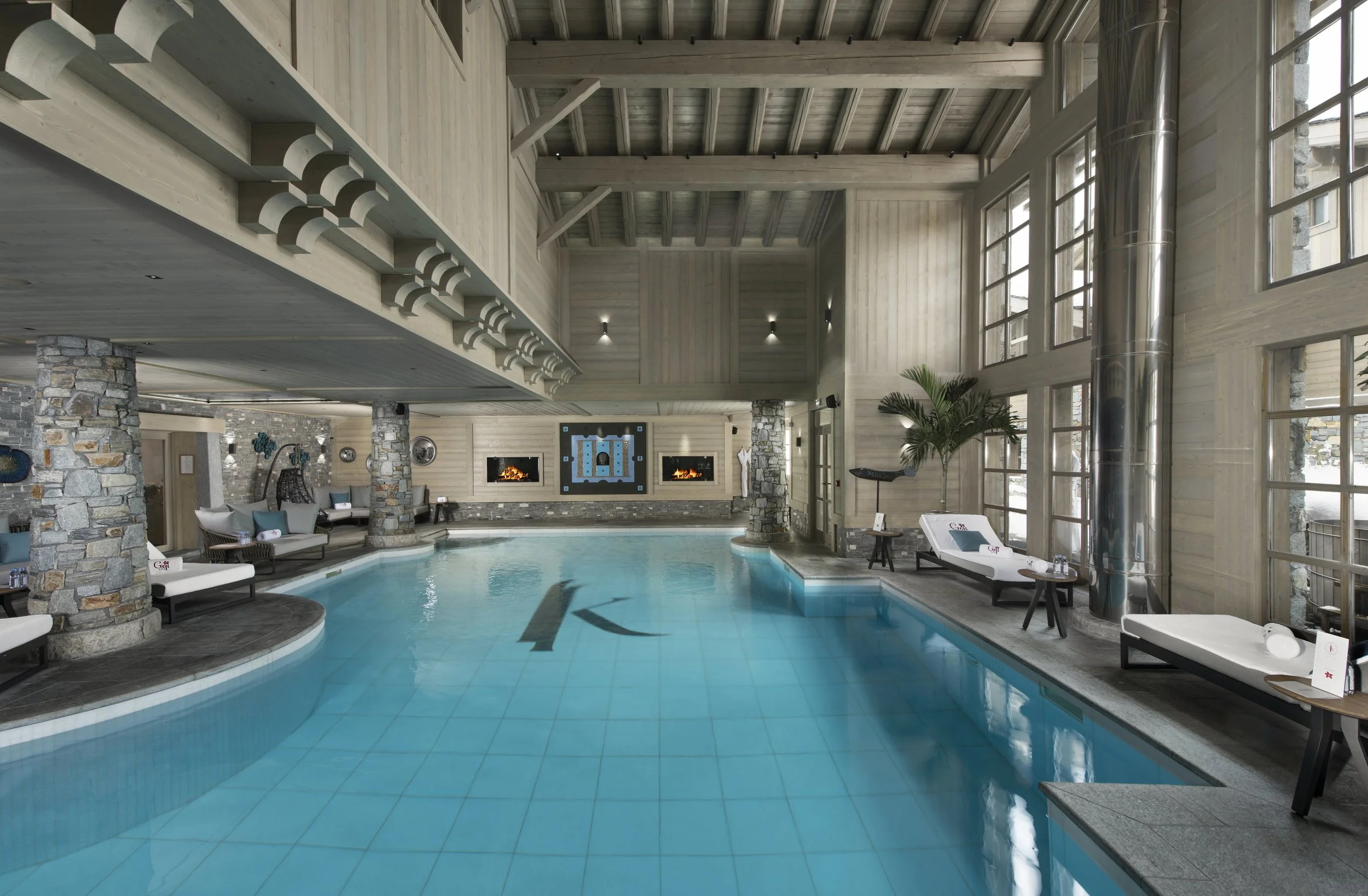 Indoor swimming pool with lounge chairs, large windows, and stone accents