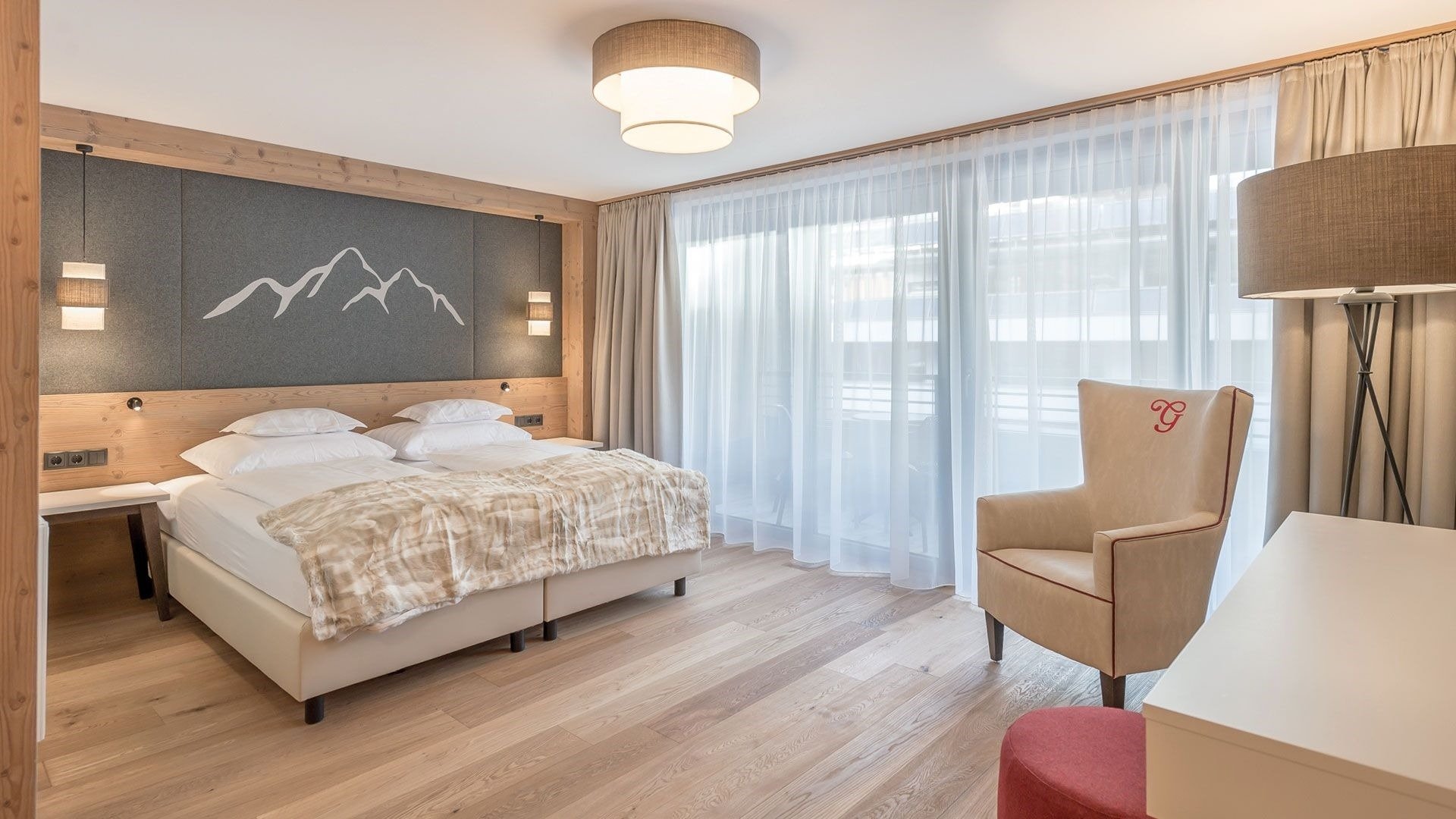 Plush double bedroom with double bed, mountain headboard, balcony, arm chair and stylish lighting.