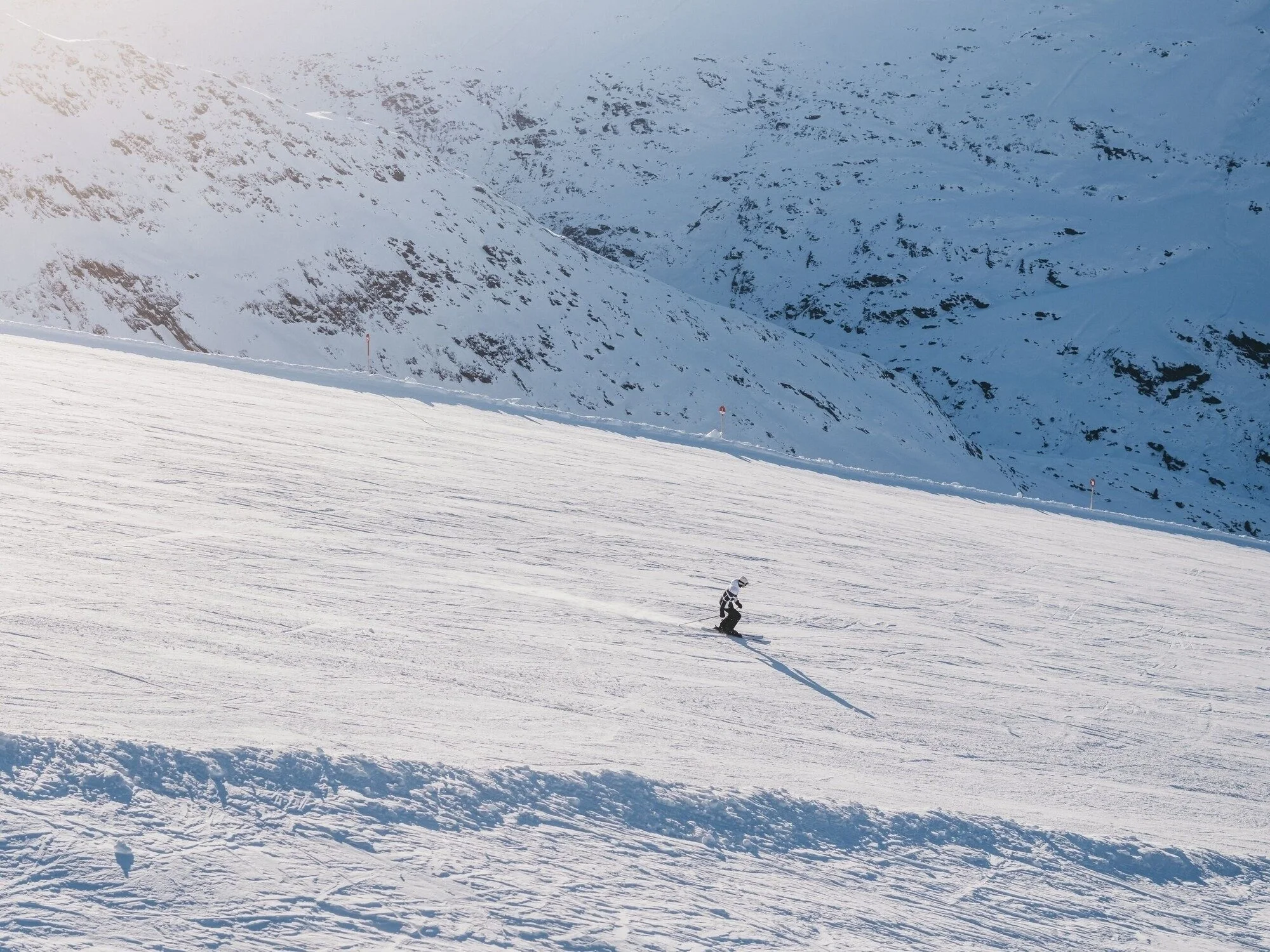Solo skier heading down the slopes with sunny conditions and fresh snowfall.