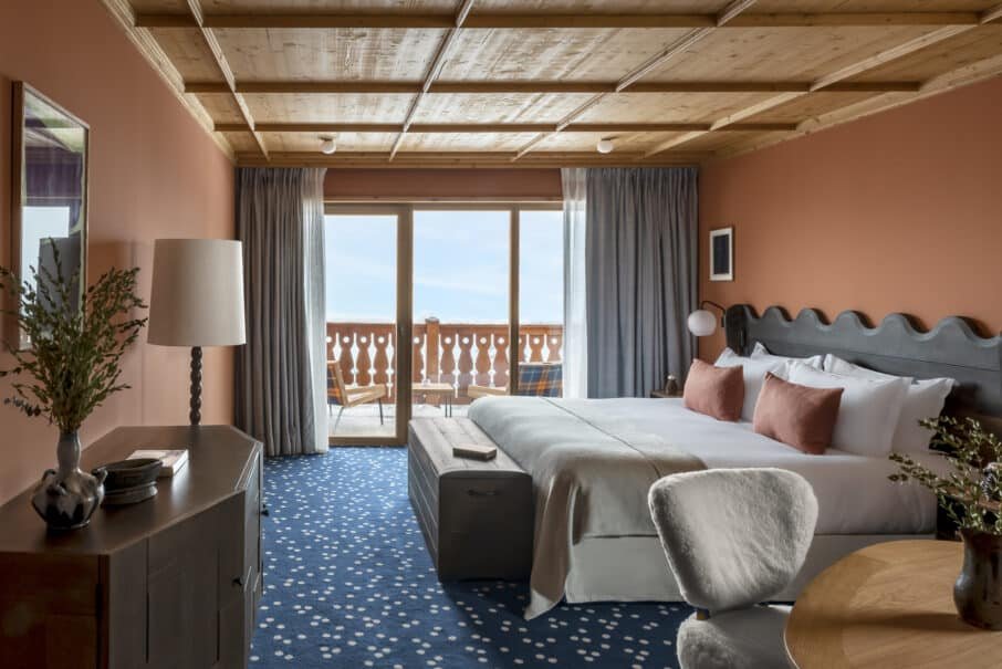 Large double bedroom with pastel colours throughout. Big terrace for the mountain views beyond. In the foreground is a coffee table with chair.