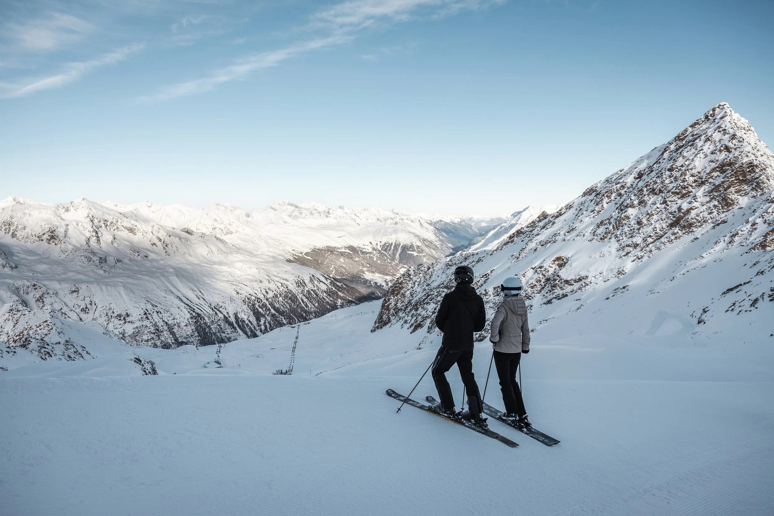 Two skiers overlooking the Obergurgl Hochgurgl terrain on a blue sunny day.